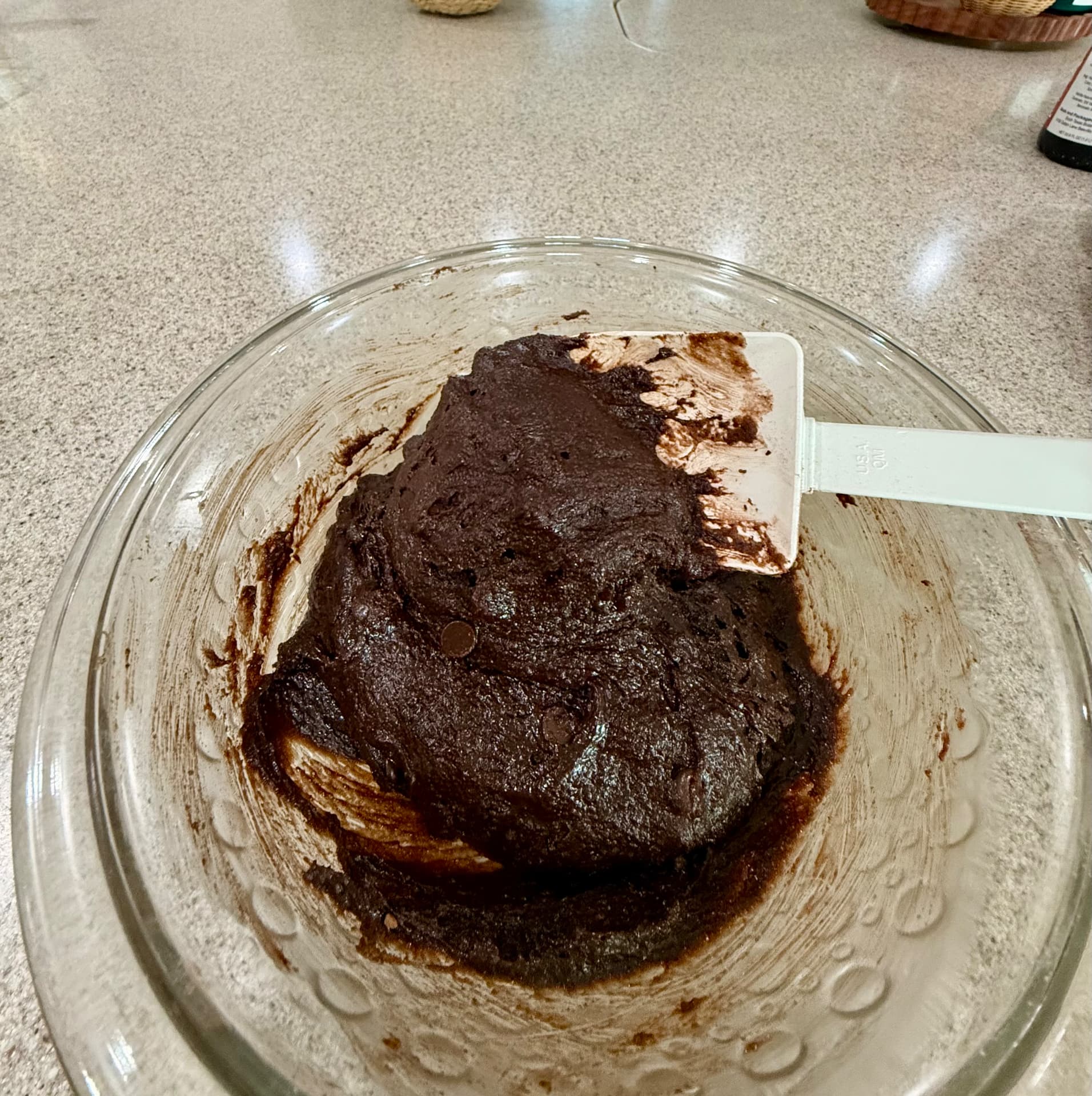Thick, fully mixed brownie batter in a glass mixing bowl with a white spatula.