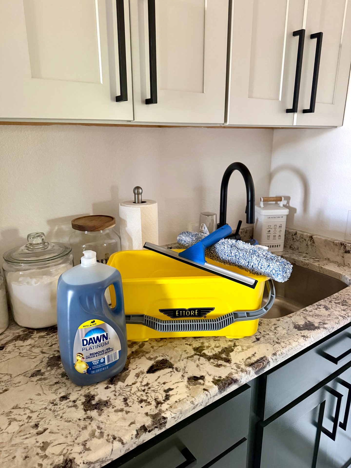 Dawn dish soap beside a yellow Ettore bucket, squeegee, and window scrubber cloths at the kitchen sink