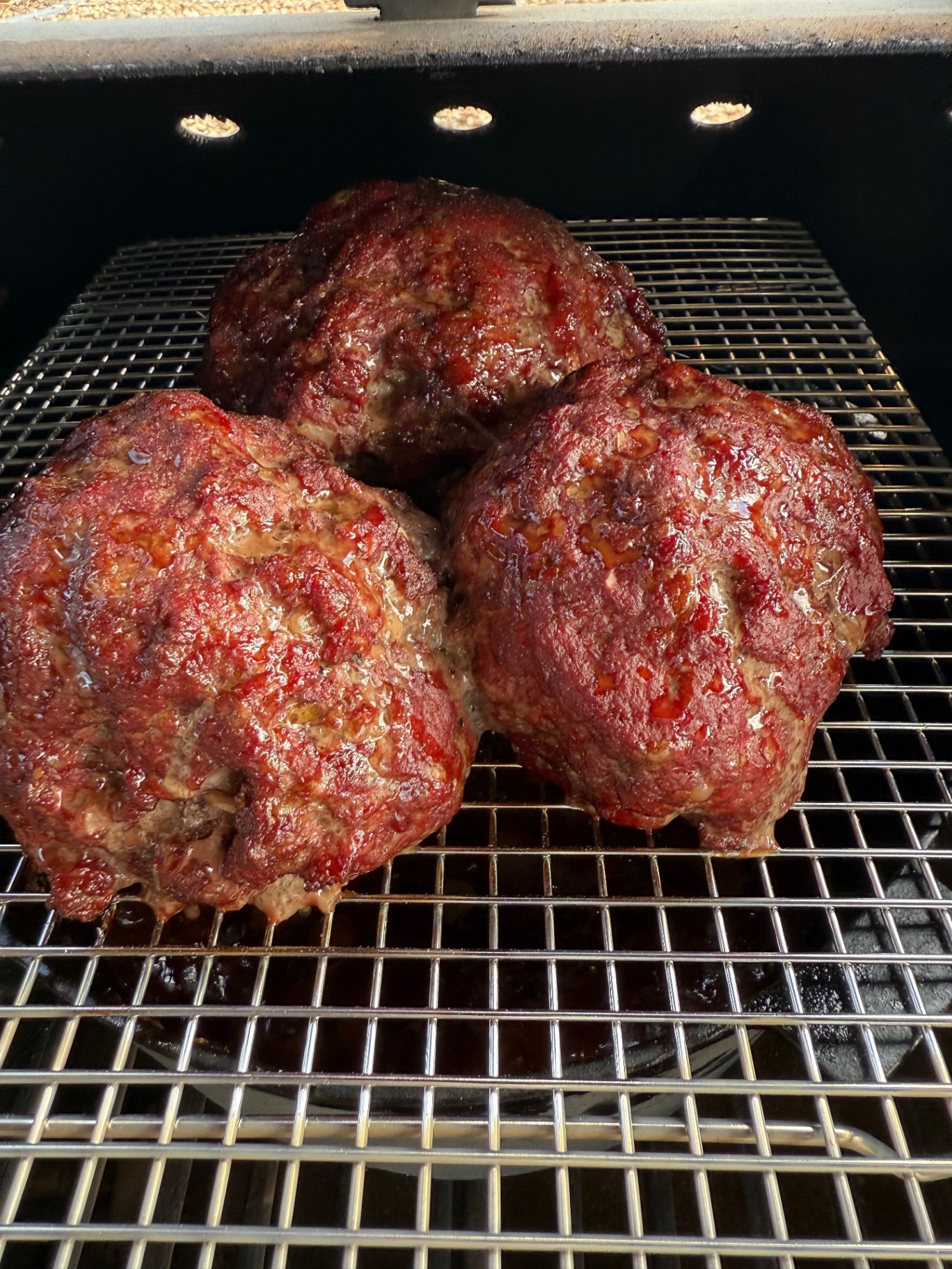 Three rounds of smoked ground beef with a deep reddish-brown crust on the smoker rack