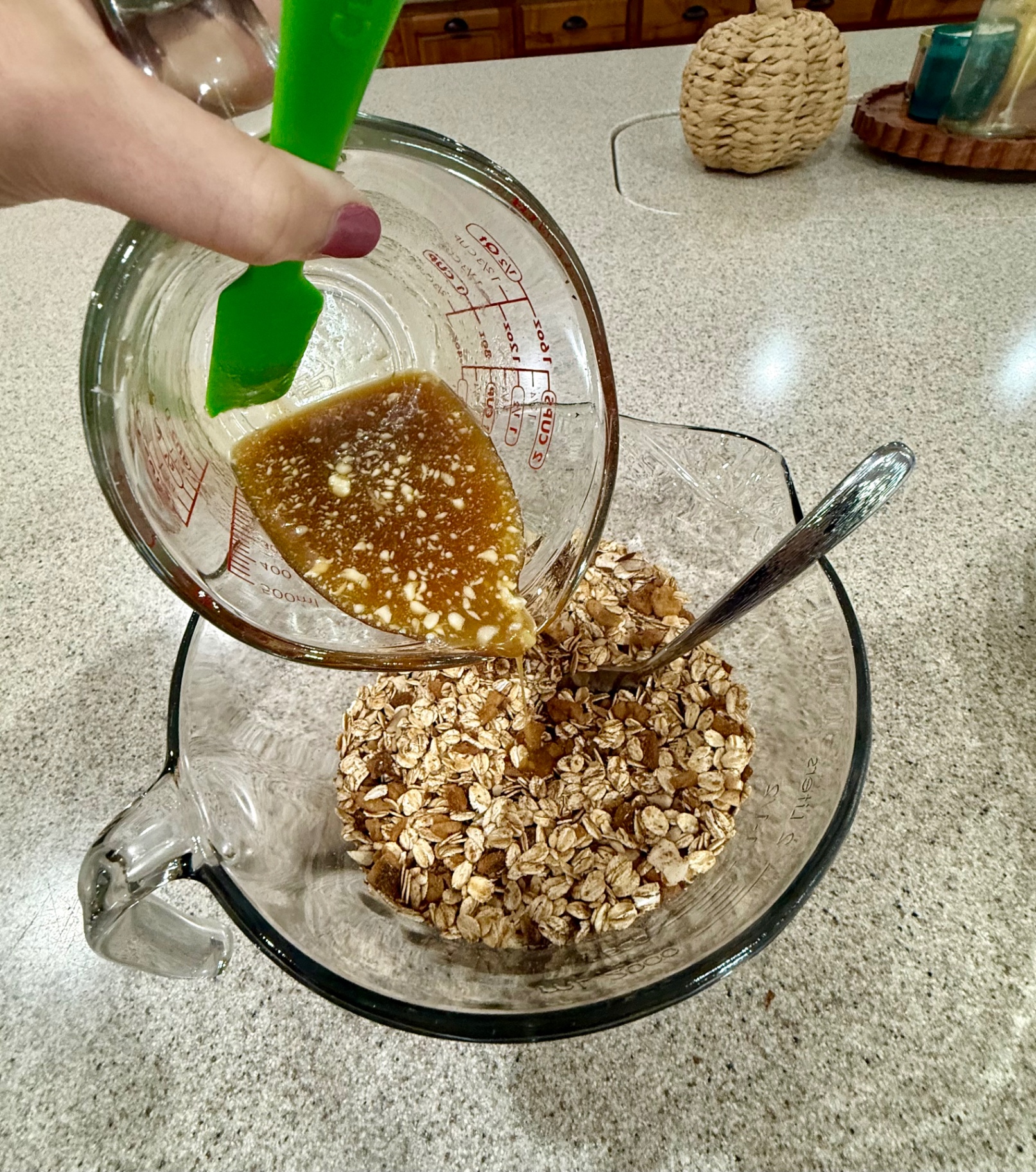 Honey, butter, and vanilla mixture being poured over the oat and nut mixture in a glass bowl.