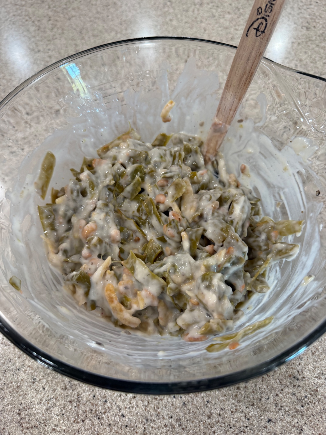 Green beans, soup, and fried onions being combined with a spatula in a glass mixing bowl.