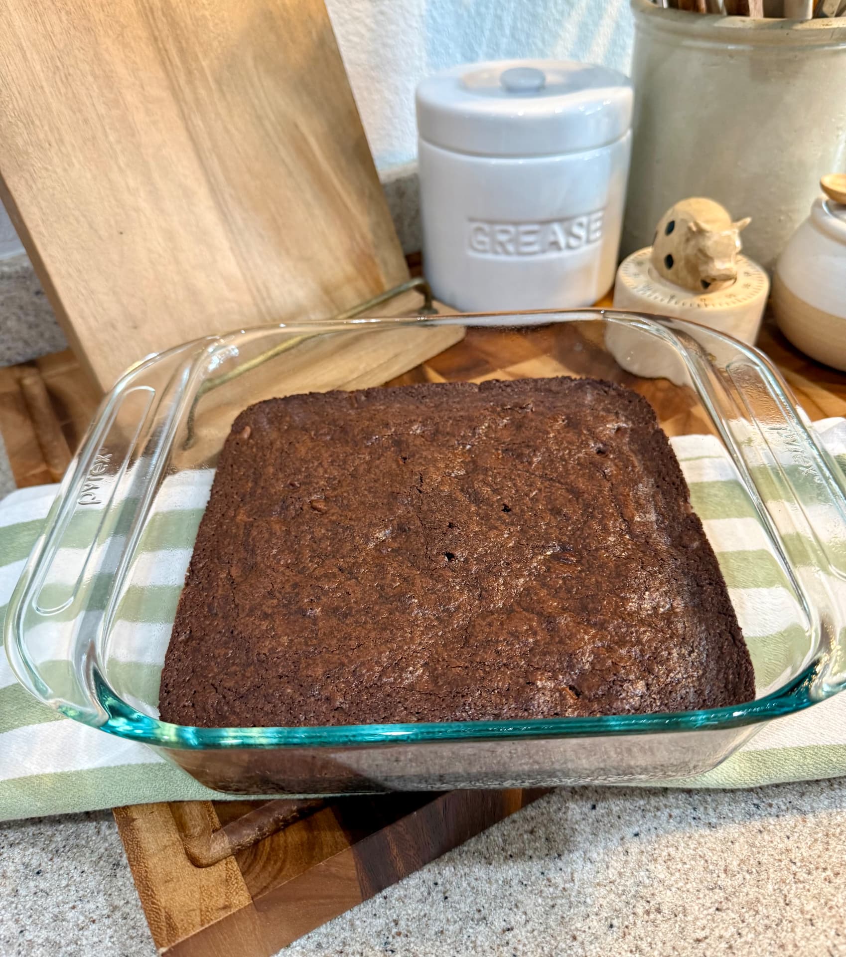 A batch of baked fudgy brownies cooling in a square glass Pyrex dish on a striped towel.