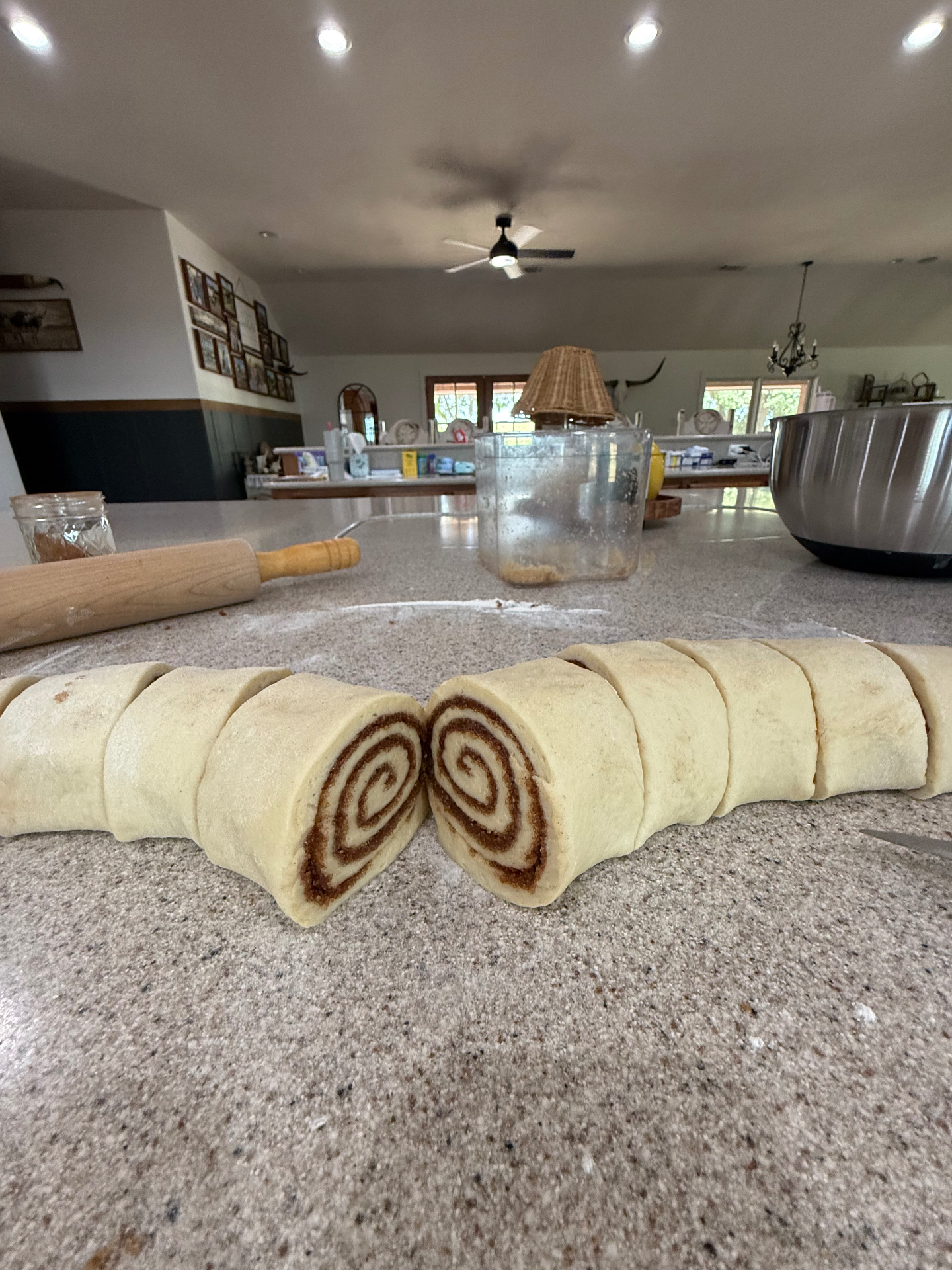 A rolled log of cinnamon roll dough sliced into rounds on a floured counter, with the cinnamon spiral showing on the cut ends