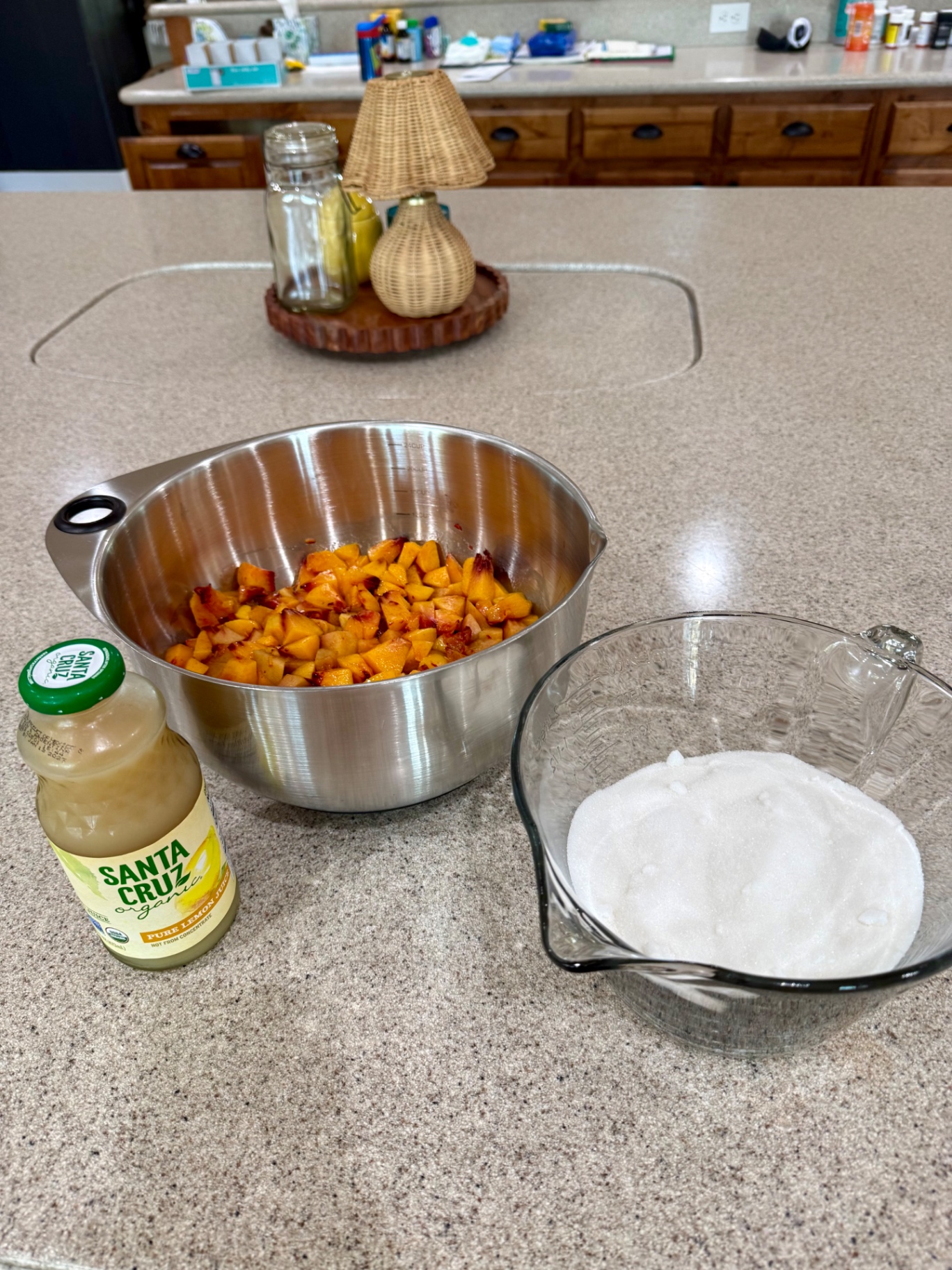 Measured peaches, granulated sugar, and a bottle of pure lemon juice arranged on the kitchen counter