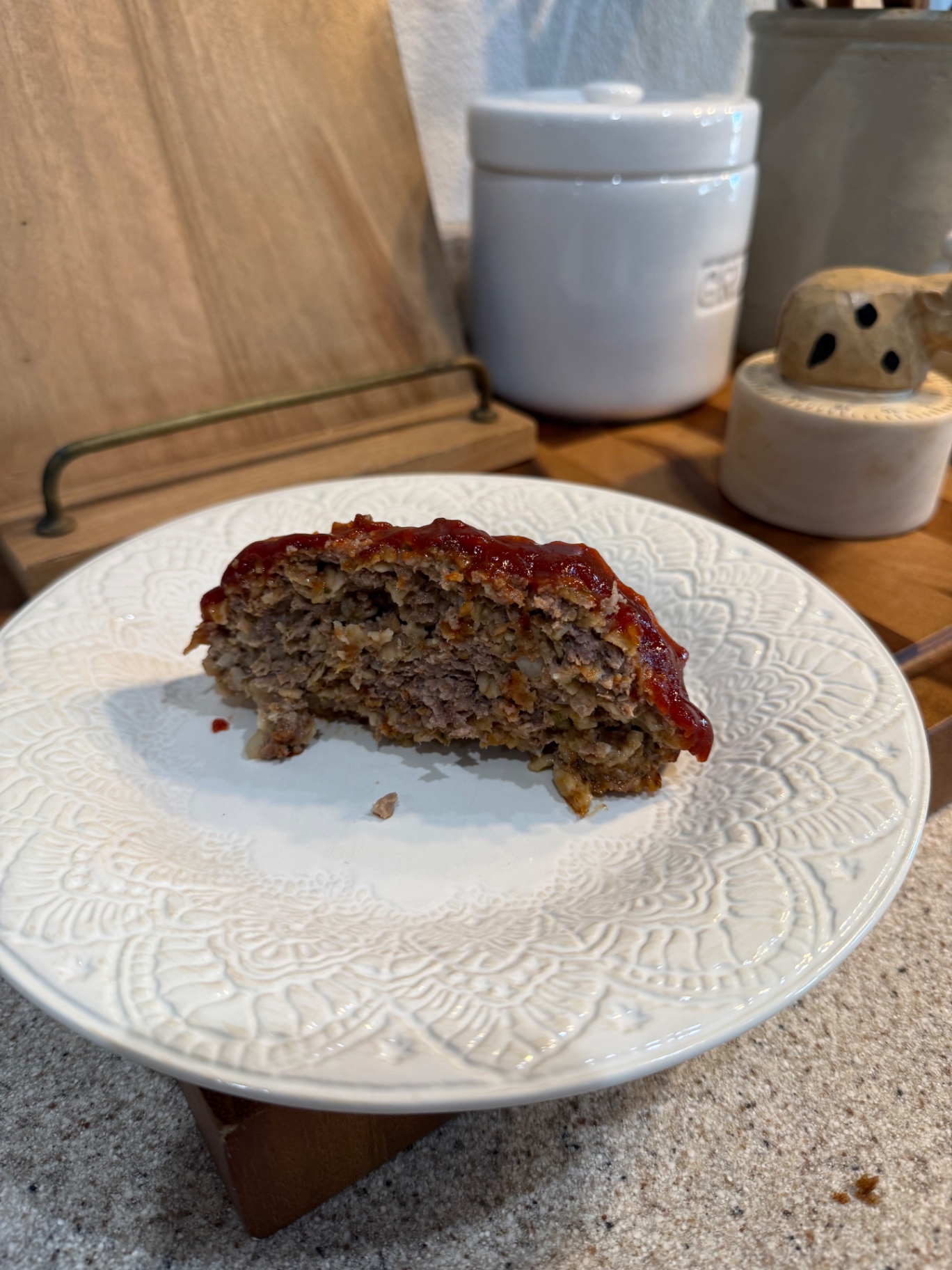 A thick slice of glazed homemade meatloaf on a white patterned plate in the Pasture Threads kitchen.