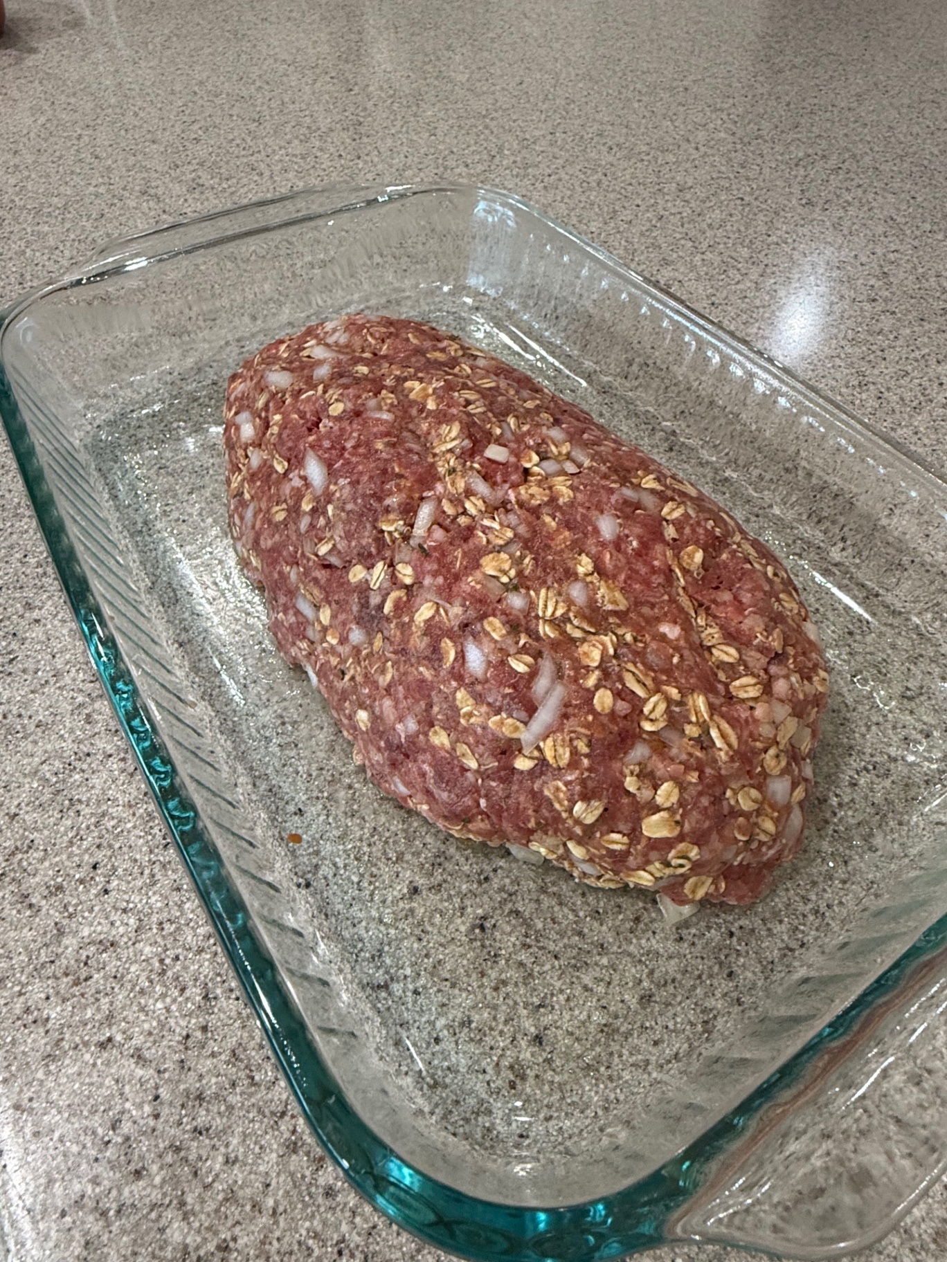 Raw shaped meatloaf in a glass baking dish before baking.