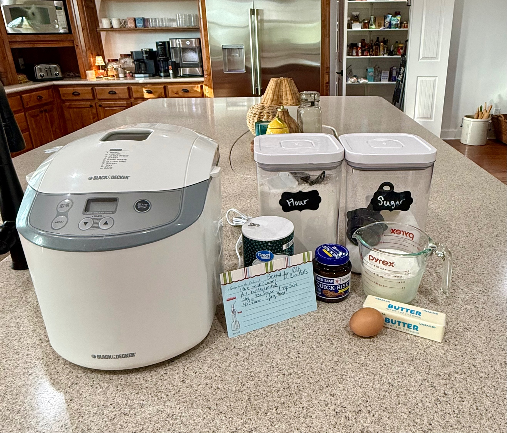 Bread machine and dinner roll ingredients arranged on the kitchen counter.
