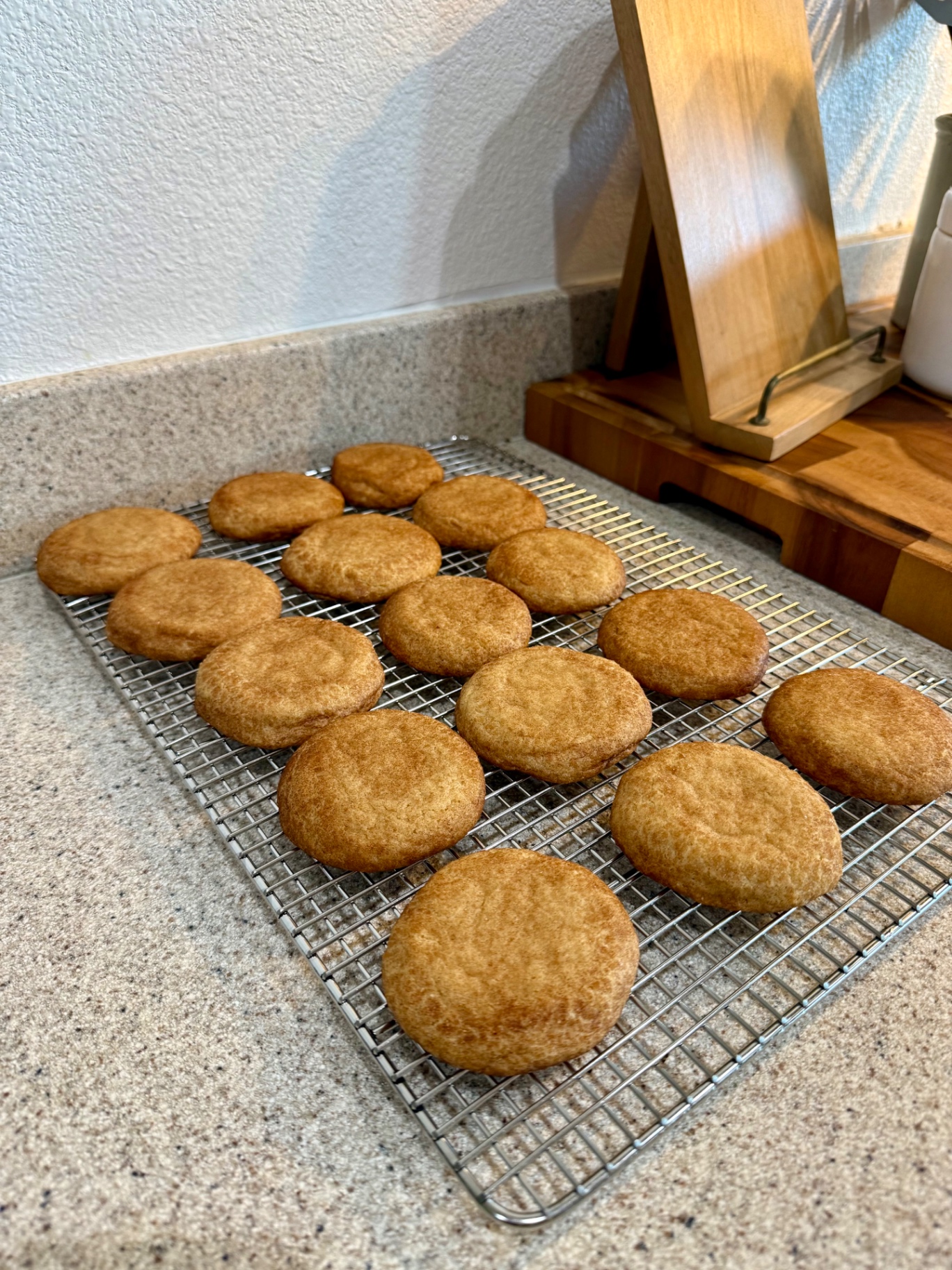 A full batch of snickerdoodles cooling on a wire rack on the kitchen counter.