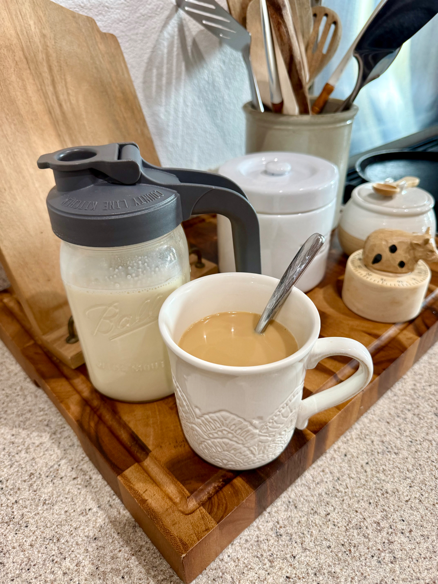 Homemade coffee creamer in a Ball mason jar with a pour lid beside a mug of coffee on a wooden board.