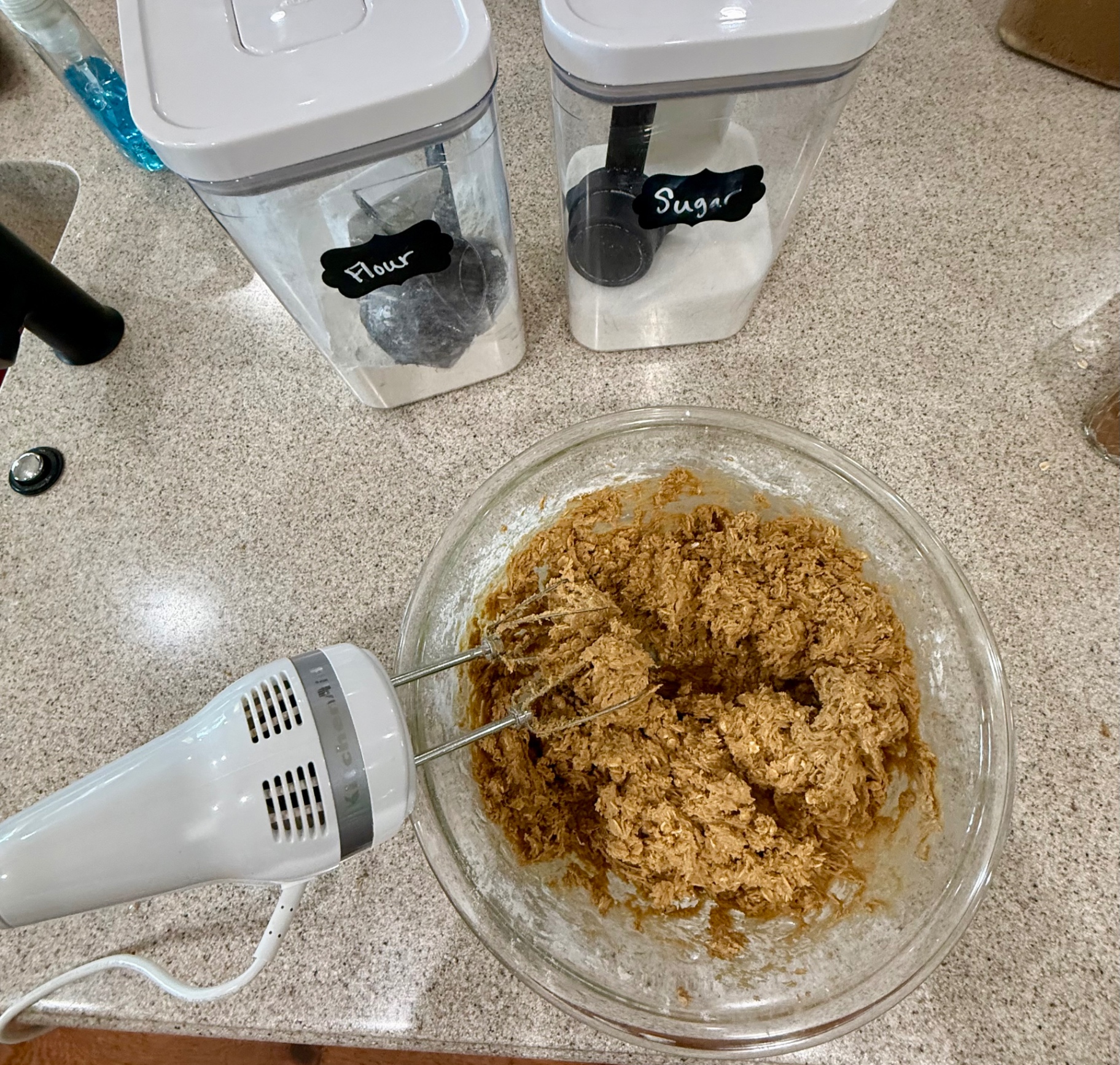 Mixed oatmeal cookie dough in a glass bowl with a hand mixer beside it.