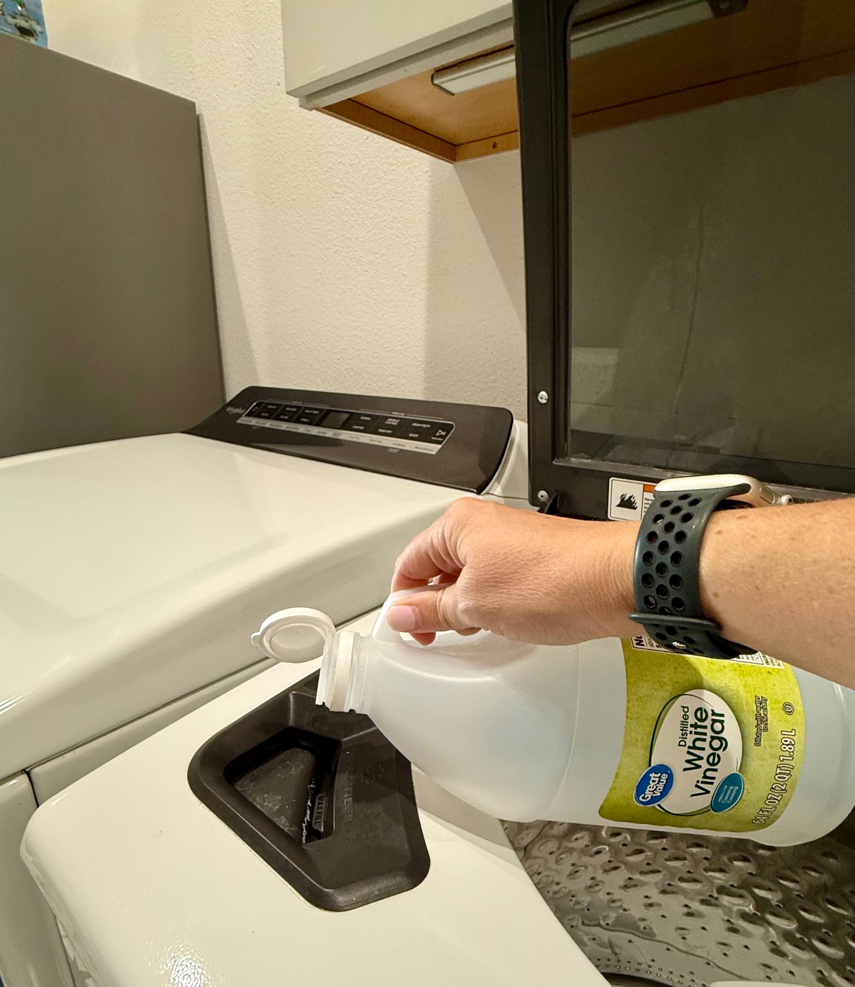 Pouring distilled white vinegar into a washing machine fabric softener dispenser.