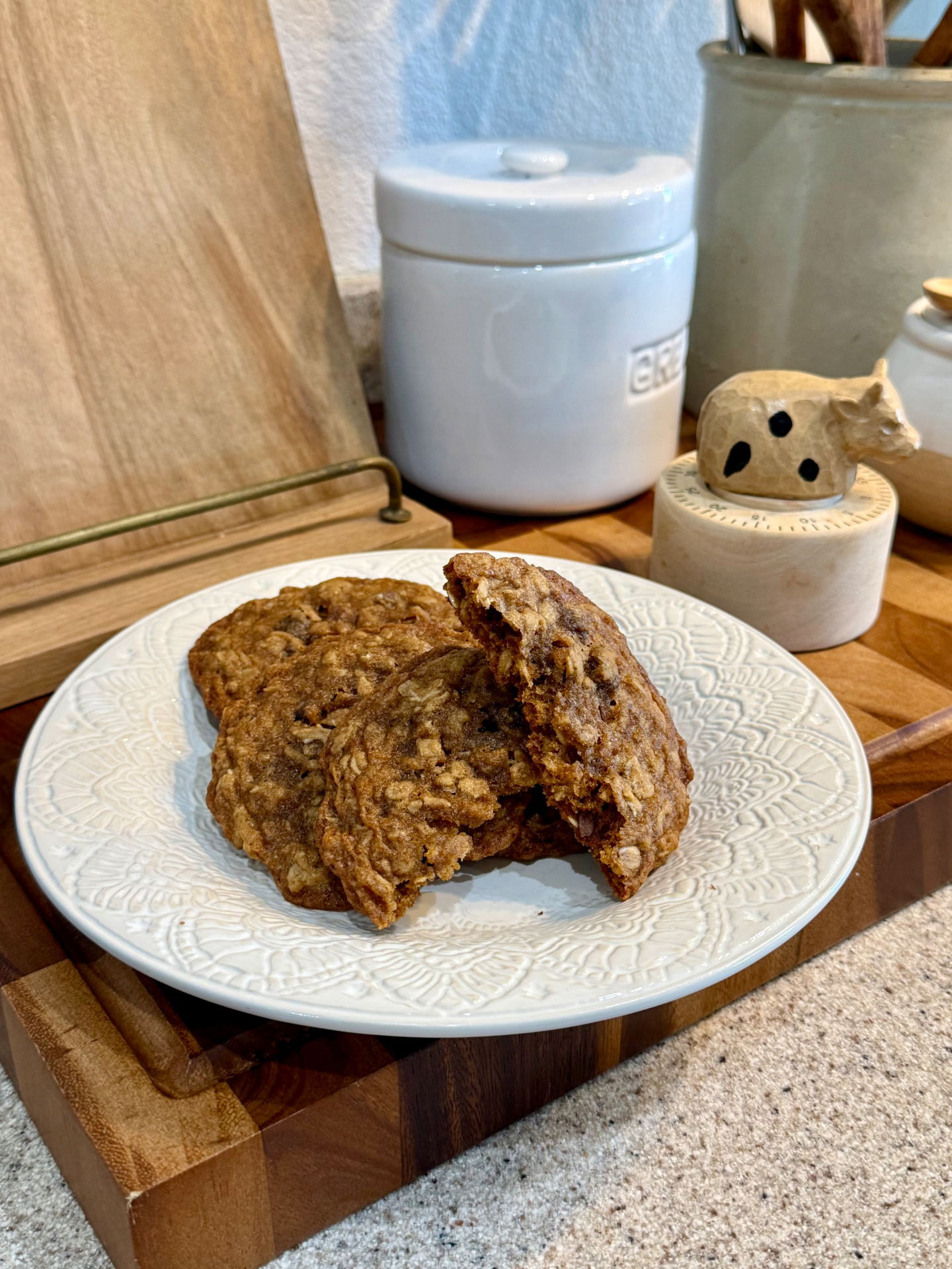 Soft oatmeal cookies on a white plate beside a ceramic cow timer on the kitchen counter.