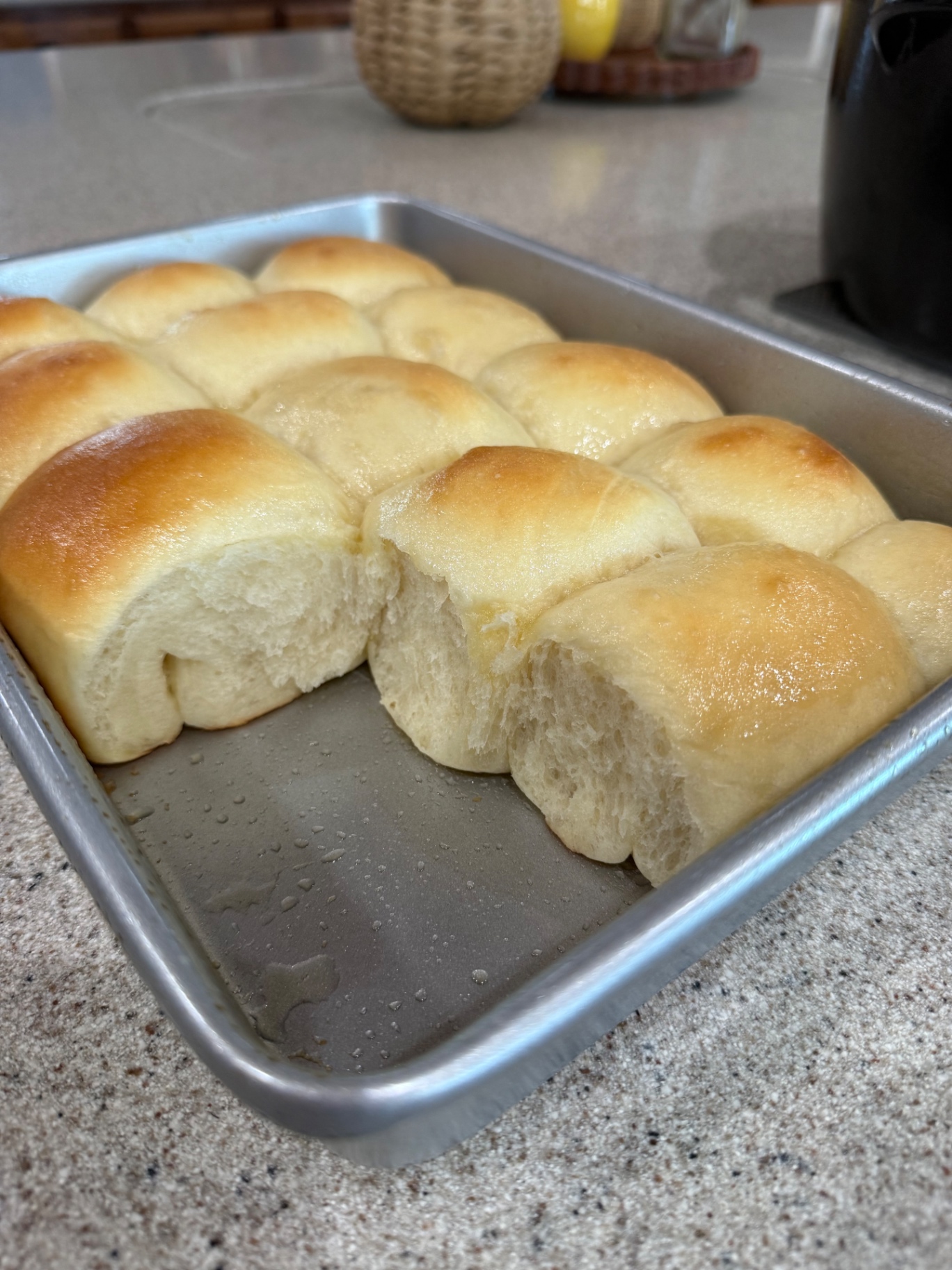 Finished pan of homemade dinner rolls with a roll pulled apart to reveal the fluffy interior.