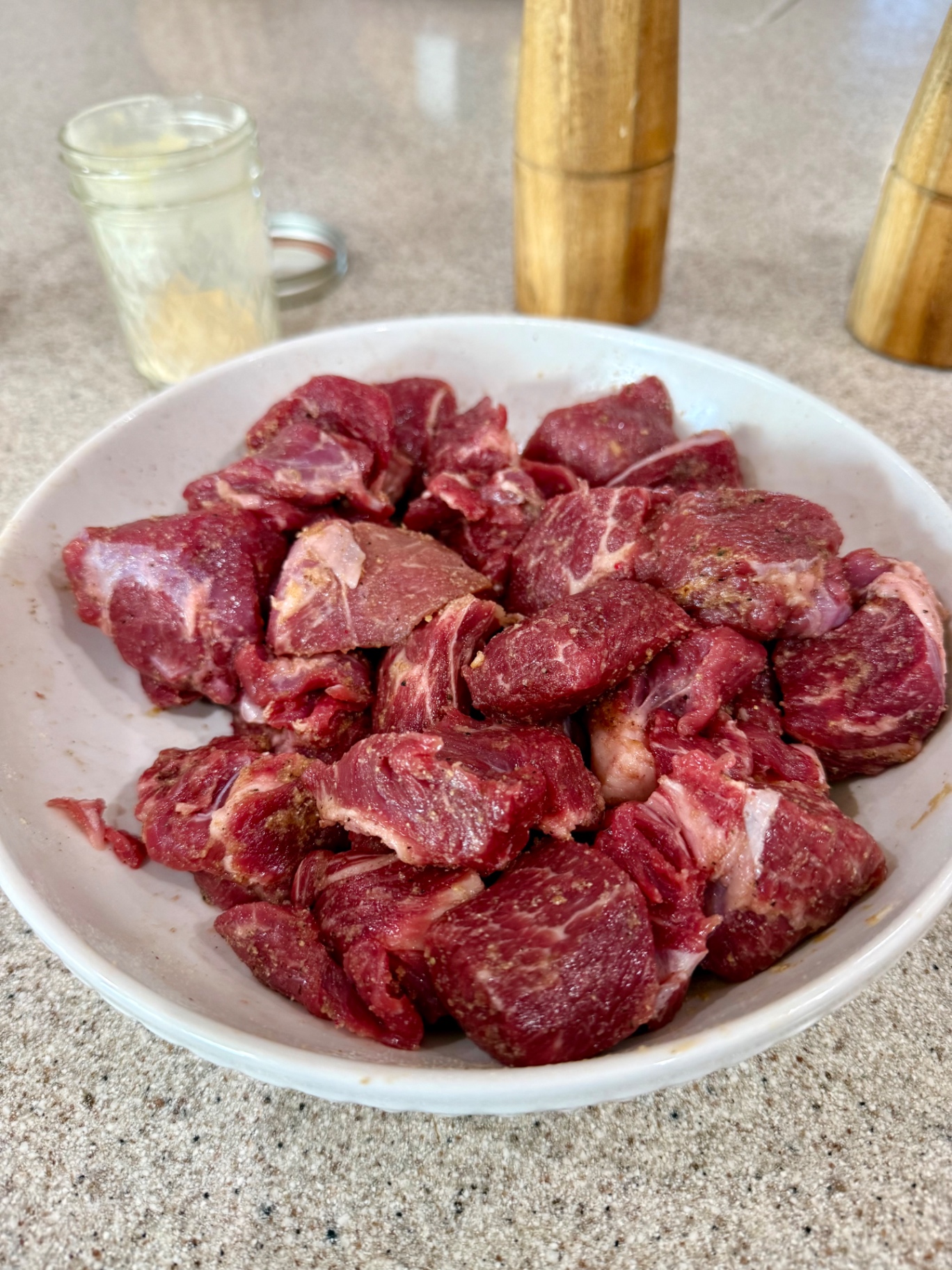Beef stew meat seasoned with salt, black pepper, and garlic powder in a white bowl.