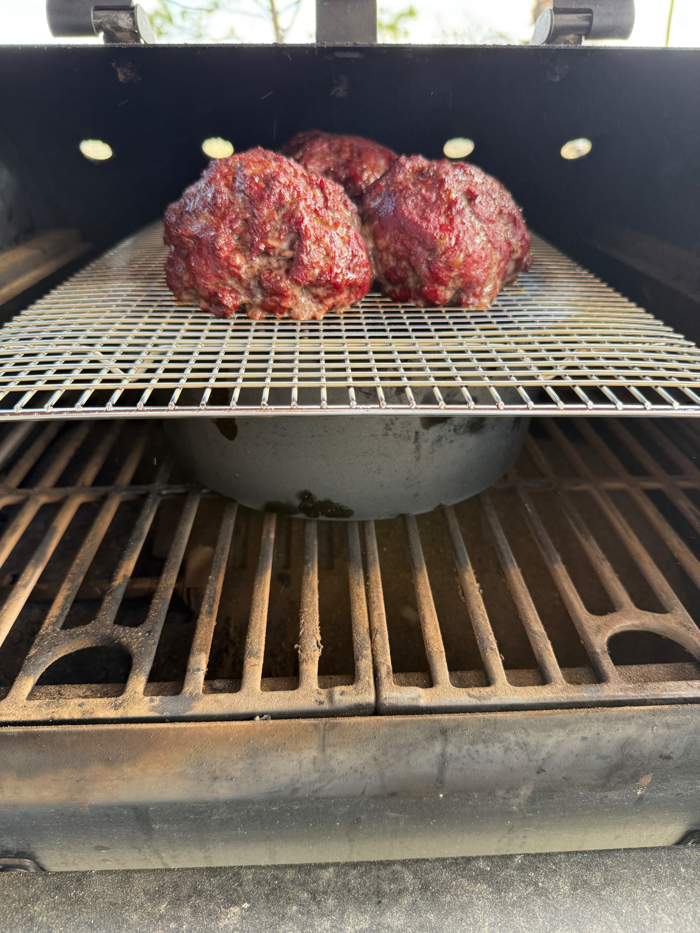 Three rounds of seasoned ground beef on a smoker rack set directly above the chili pot