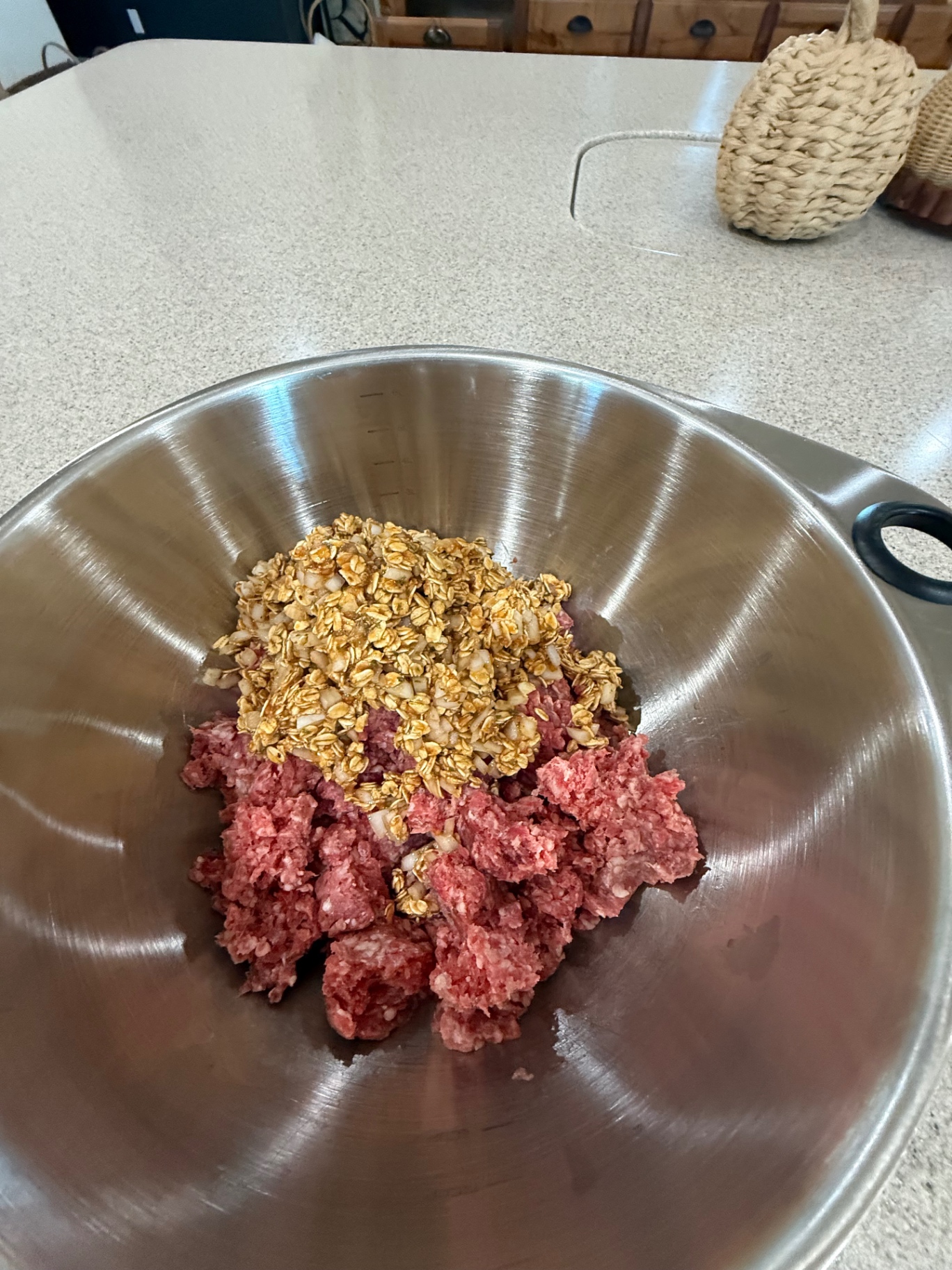 Ground beef in a stainless bowl topped with the soaked oat and onion mixture before mixing.