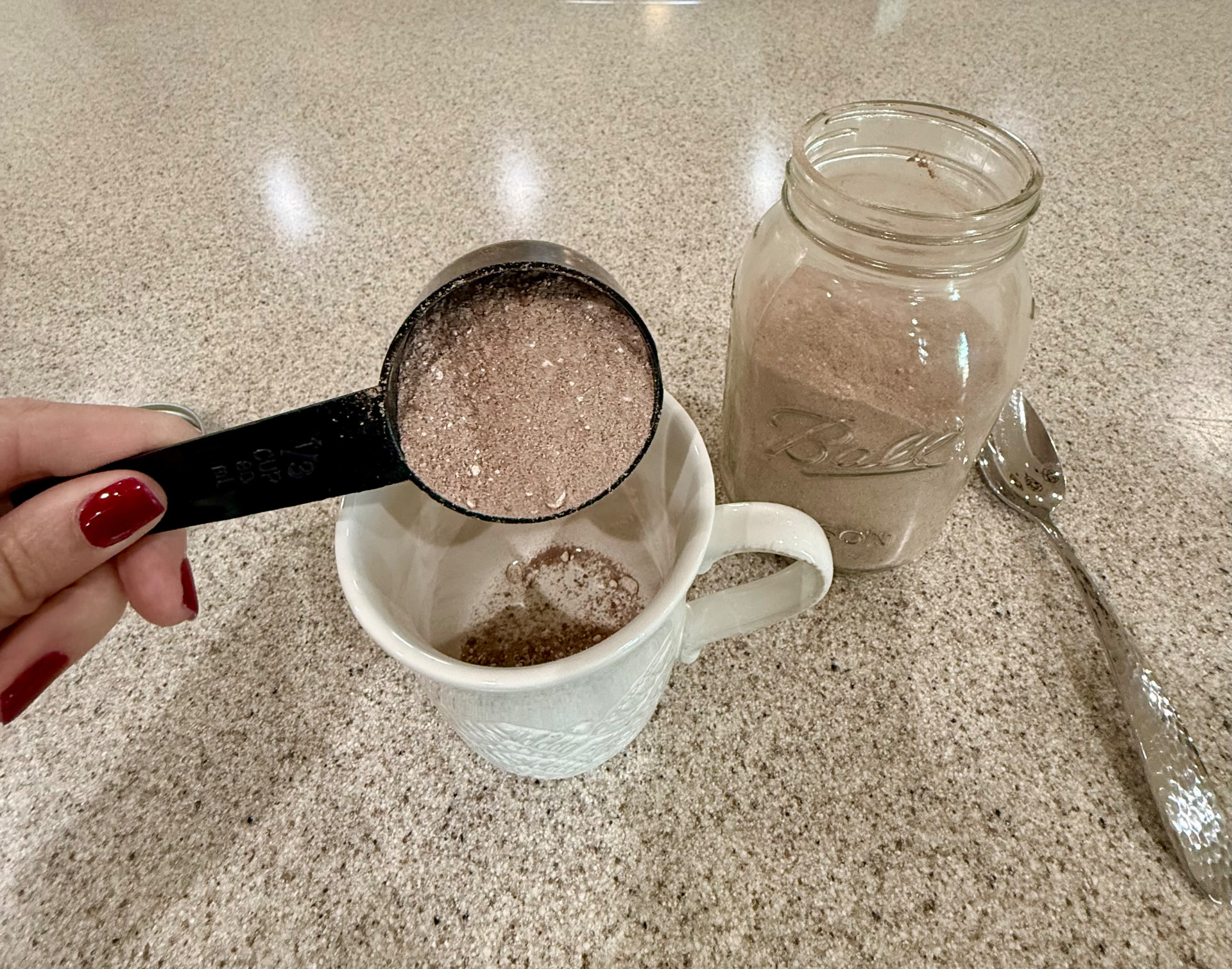 Measuring the dry hot cocoa mix into a white mug beside the mason jar.