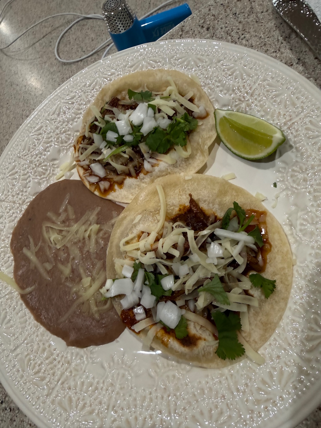 Two birria tacos on a white plate with beans and a lime wedge