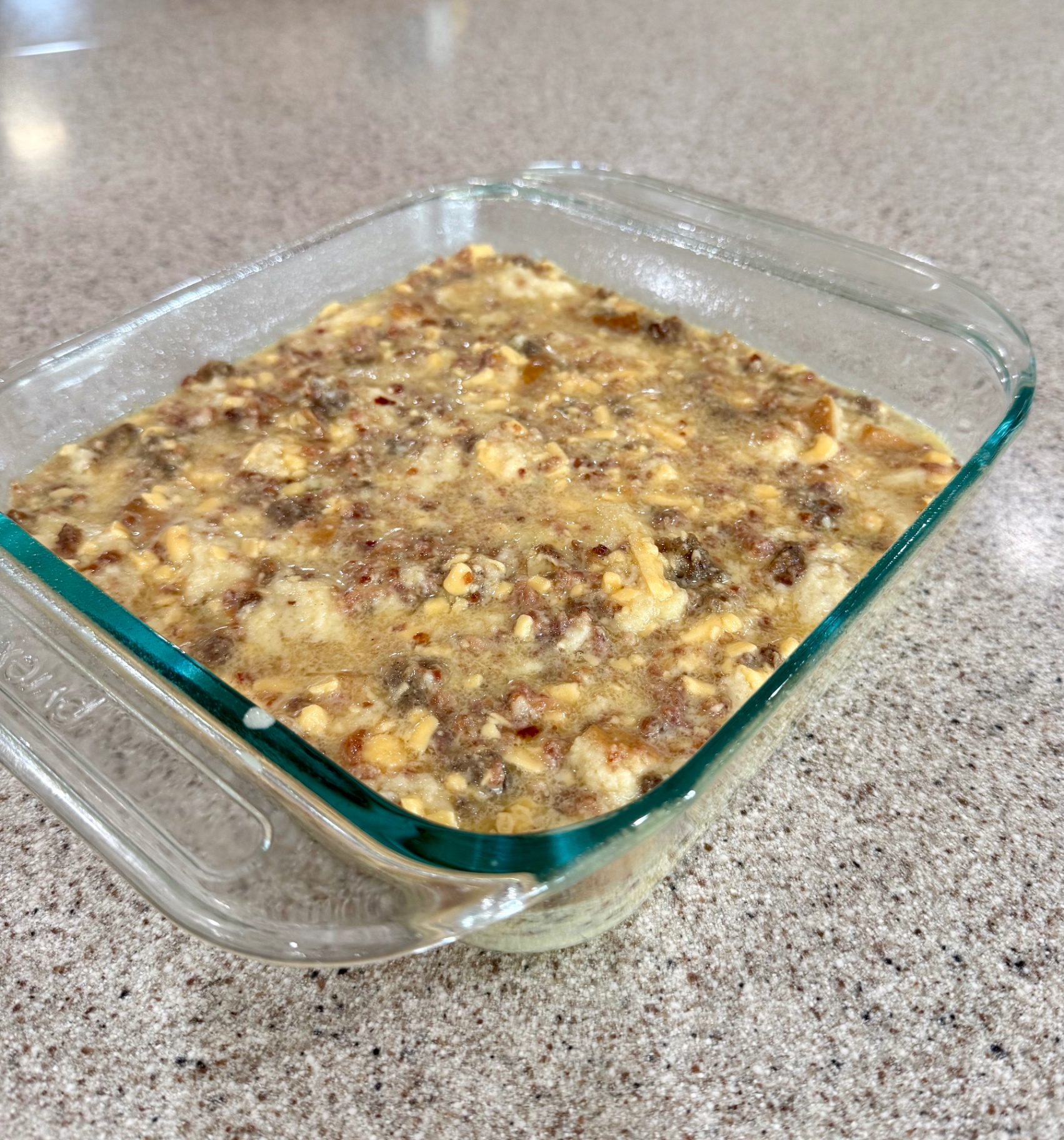 Uncooked sausage, egg, and bread casserole mixture poured into a glass baking dish on the counter