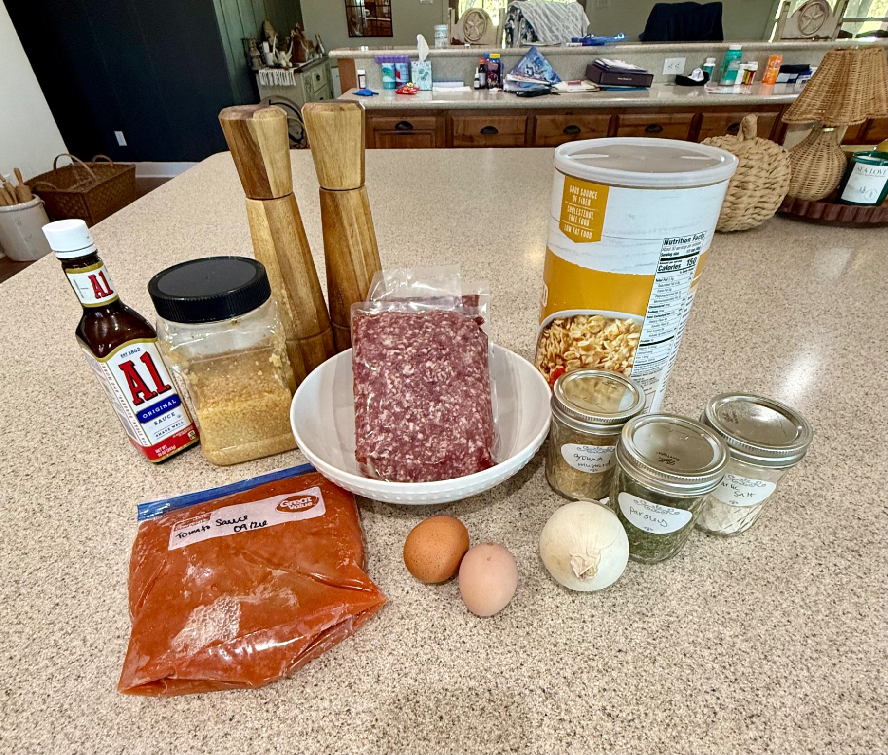 Meatloaf ingredients on the counter: ground beef, eggs, onion, oats, A.1. sauce, tomato sauce, garlic, and seasonings.