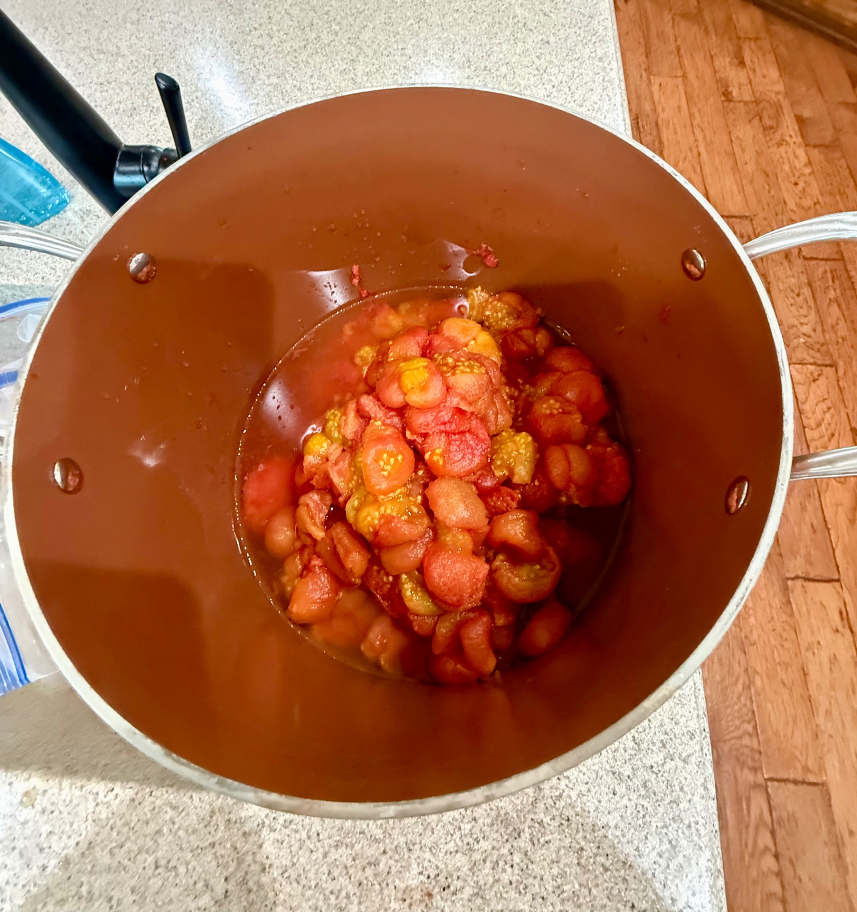 Peeled garden tomatoes simmering in a large stockpot for homemade freezer tomato sauce.