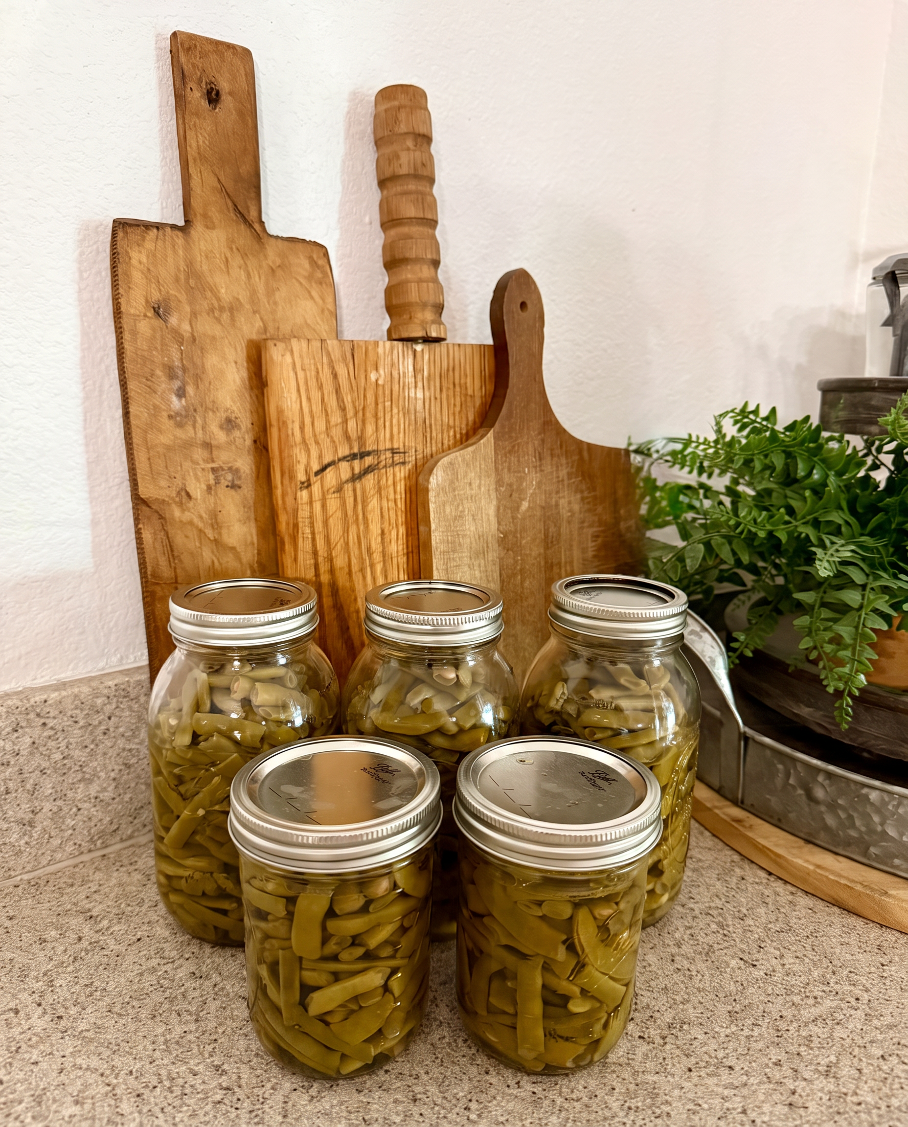 Quart jars of home-canned green beans cooling on the counter in front of vintage wooden cutting boards