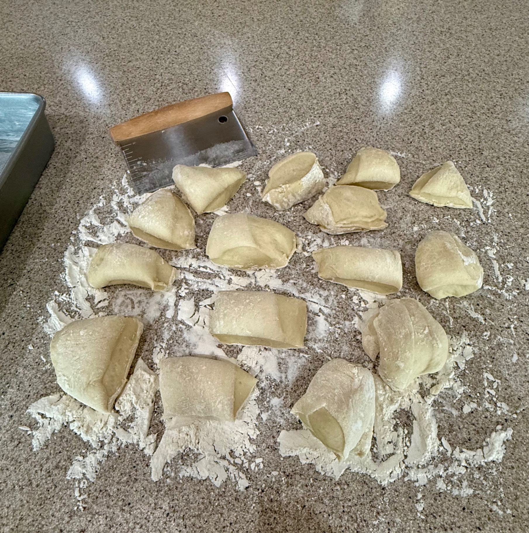 Dinner roll dough divided into pieces on the floured counter beside a dough cutter.
