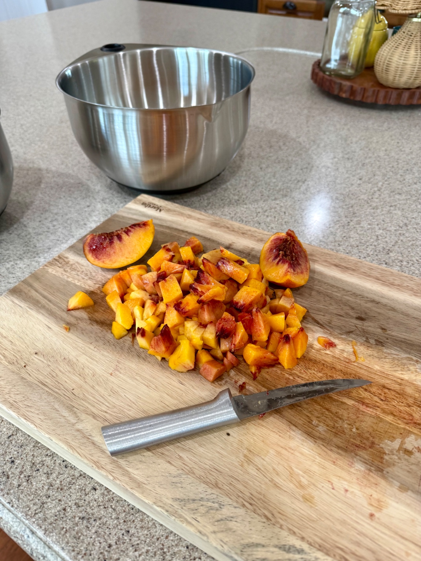 Peeled yellow peaches being diced on a wooden cutting board with a small paring knife