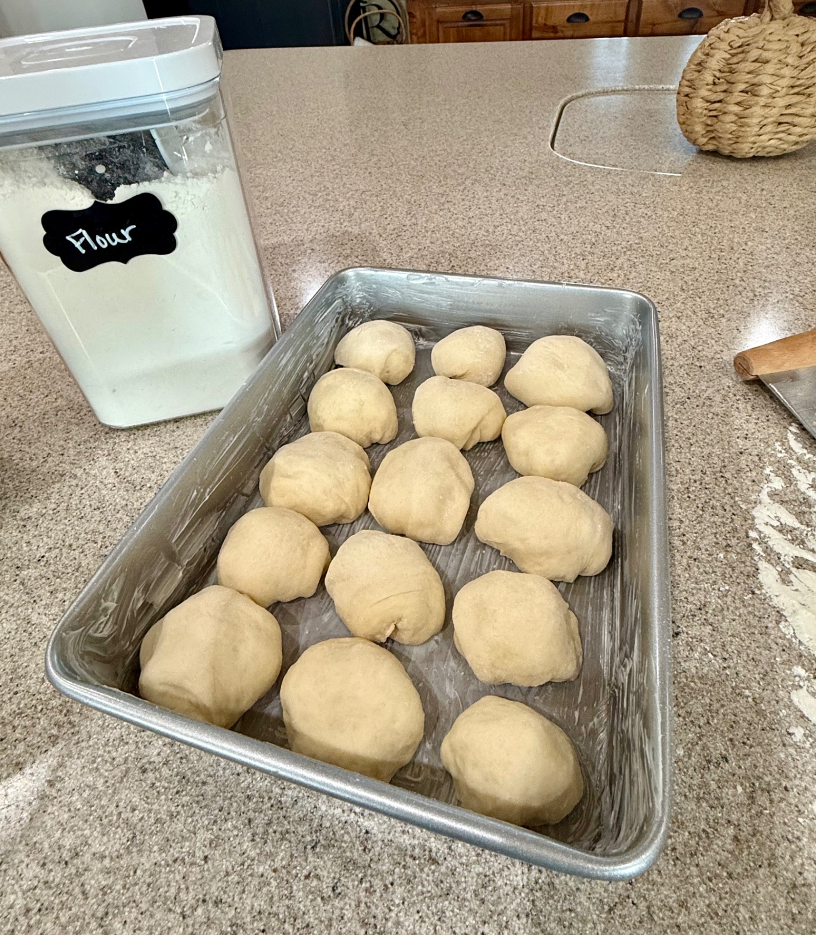 Fifteen shaped dinner rolls arranged in a greased rectangular pan on the kitchen counter.