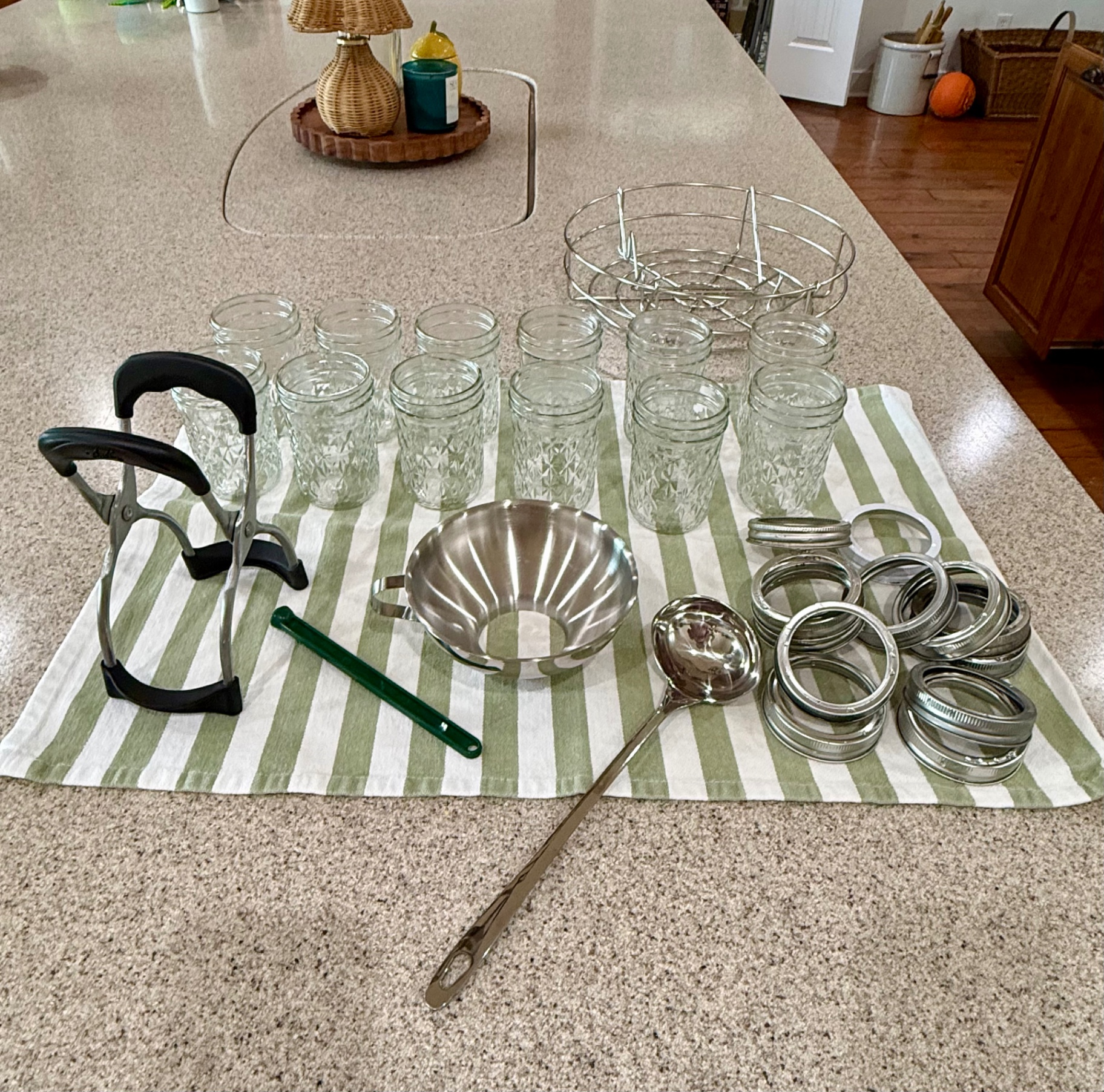 Water-bath canning jars, rings, rack, funnel, ladle, and magnetic lid lifter arranged on a striped towel