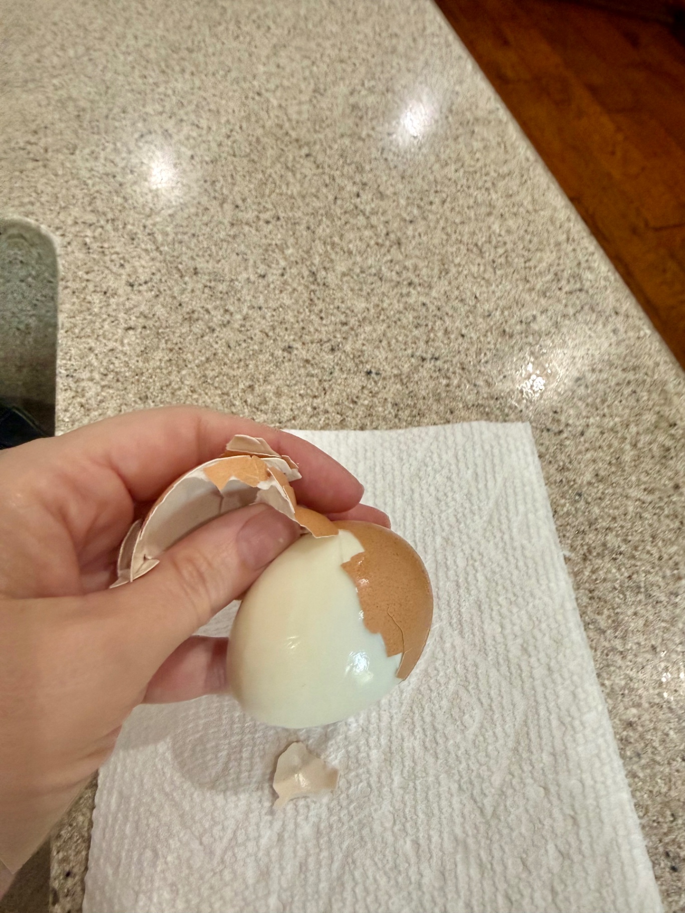 Peeling the brown shell from a cooked egg over a paper towel.