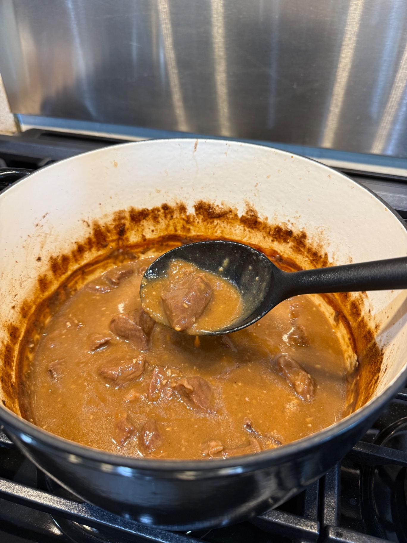 A spoon lifting a cooked beef tip from the finished gravy in the Dutch oven.