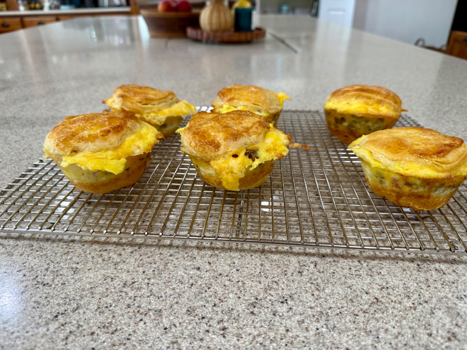 Loaded breakfast biscuits filled with eggs, cheese, and breakfast meat cooling on a rack.