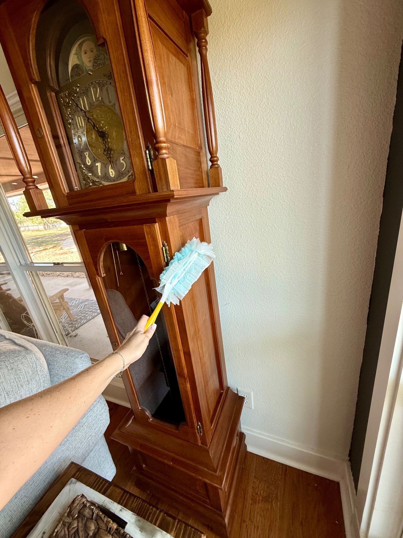 Dusting the wooden case of a grandfather clock with a duster