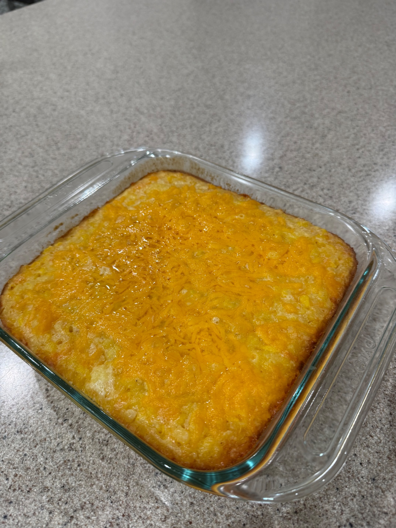 Finished cheesy corn casserole with melted golden cheddar in a glass baking dish.