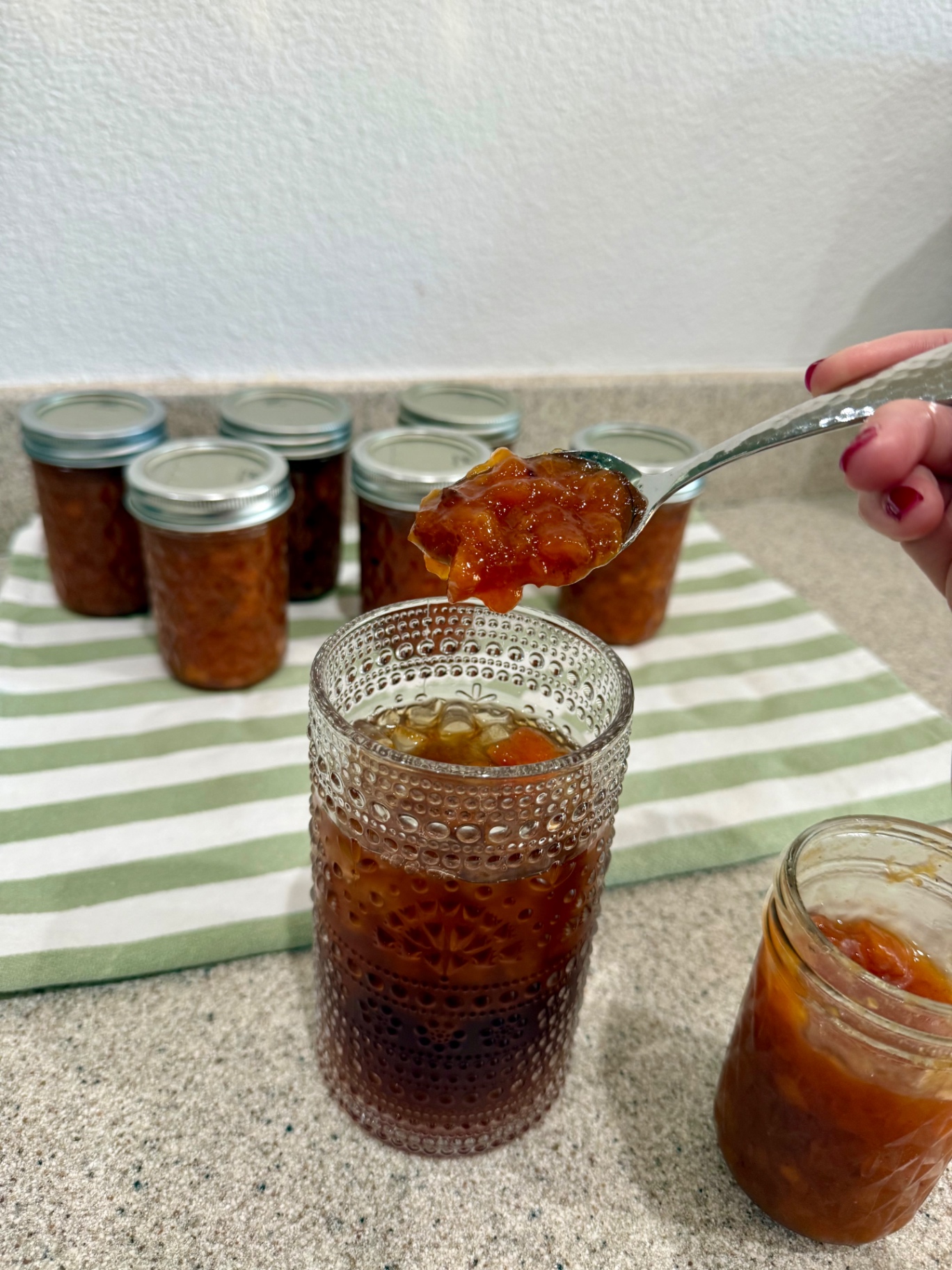 A spoonful of homemade peach topping held over a glass of iced tea