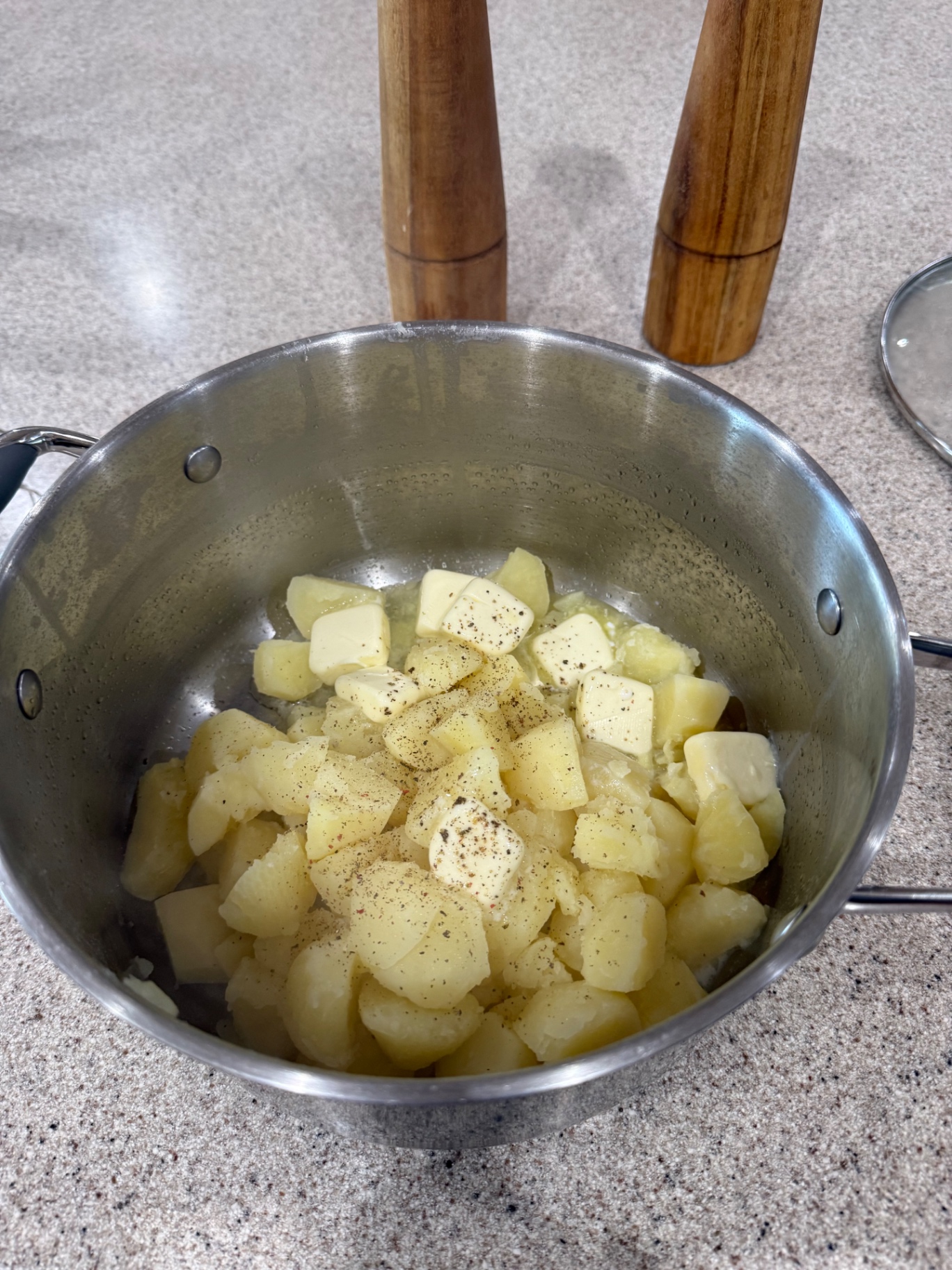 Cooked potato chunks in the pot with butter and seasoning added.