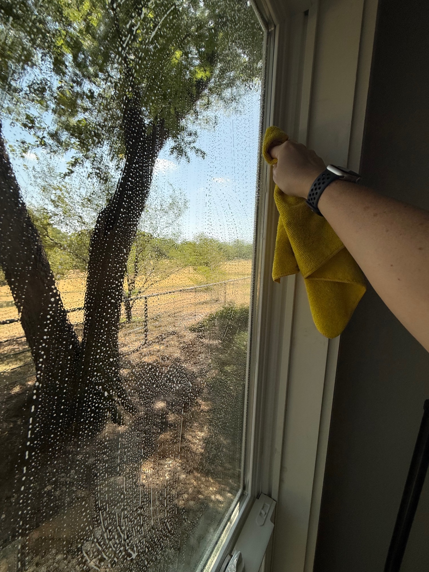 Wiping water from the edge of a window with a microfiber towel.