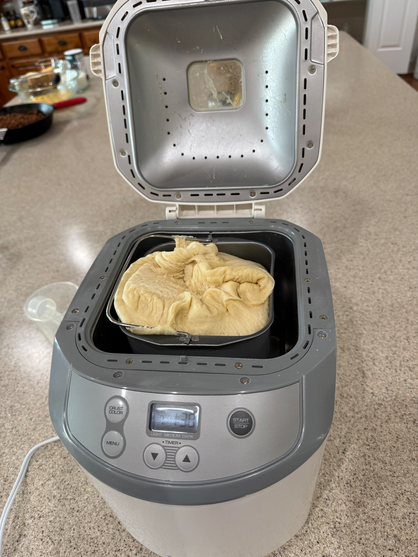 Soft roll dough risen to the top of the pan inside an open bread machine on the kitchen counter