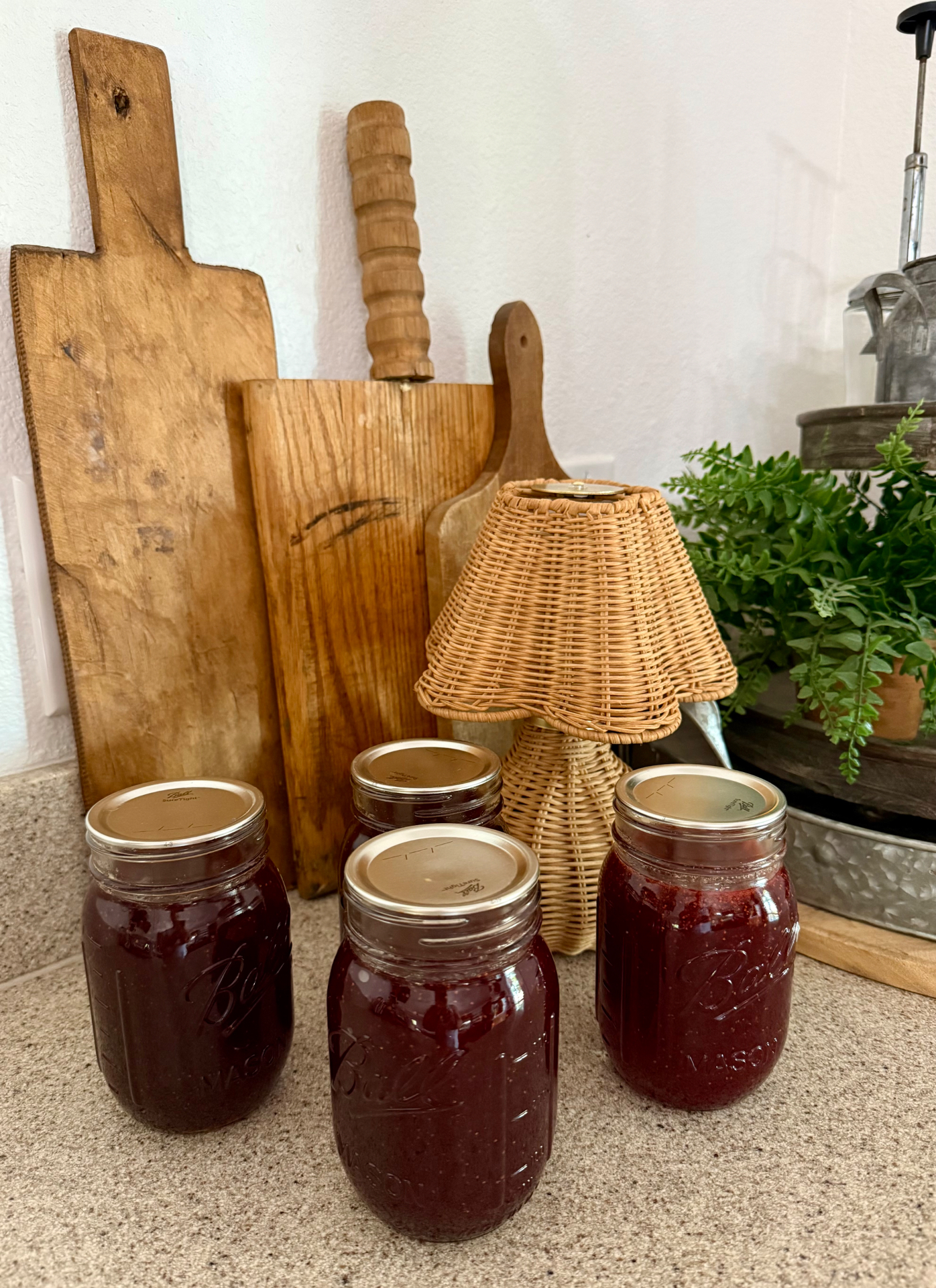 Four jars of homemade strawberry jam on the kitchen counter with wooden cutting boards behind them