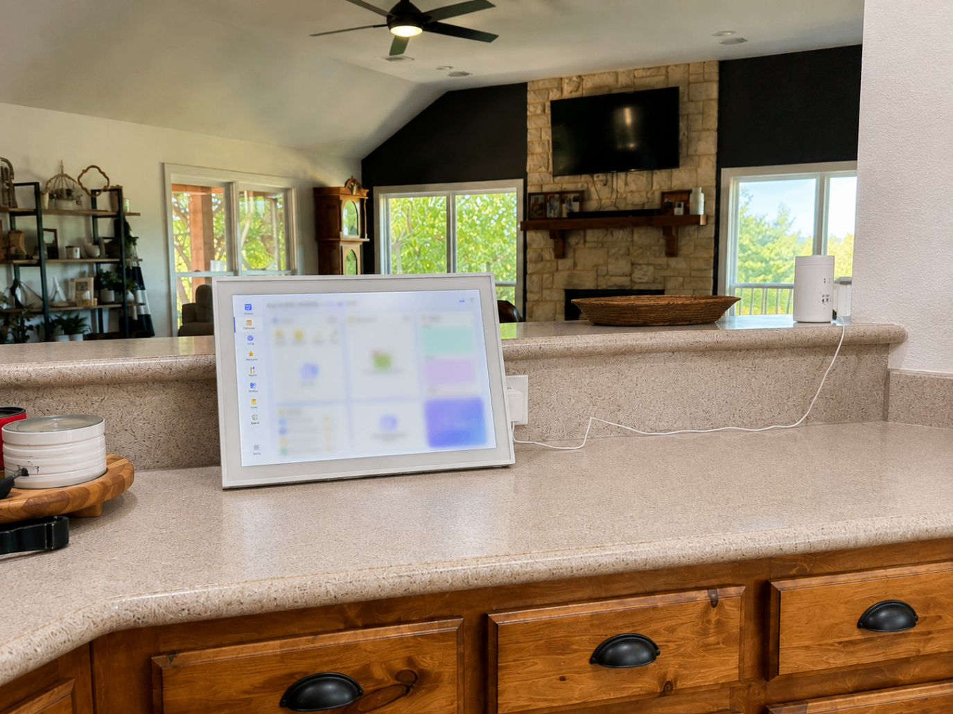 A large digital family calendar display sitting on a kitchen counter with the living room beyond