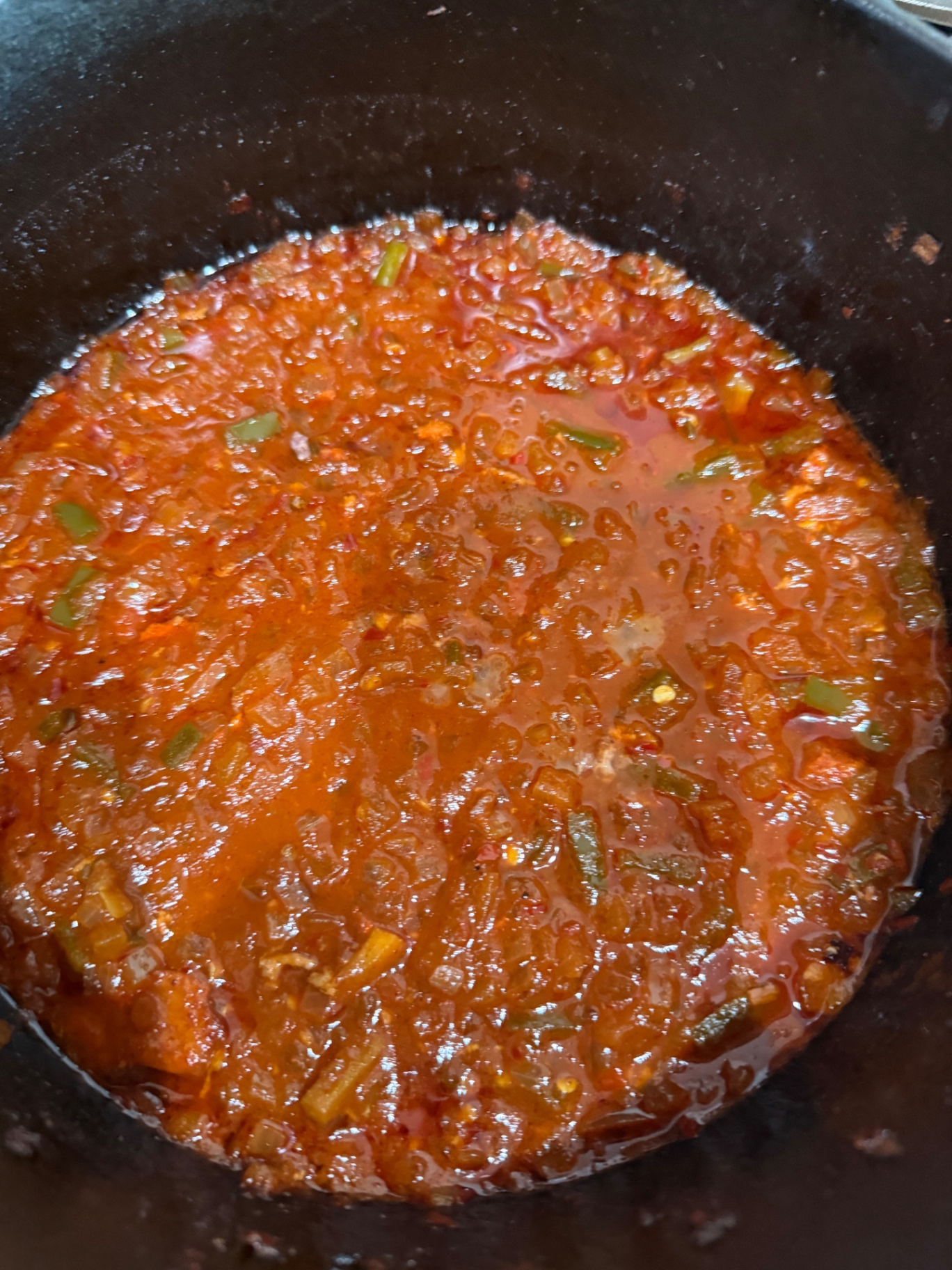 Chili base of crushed tomatoes, onion, and diced jalapeños simmering in a Dutch oven