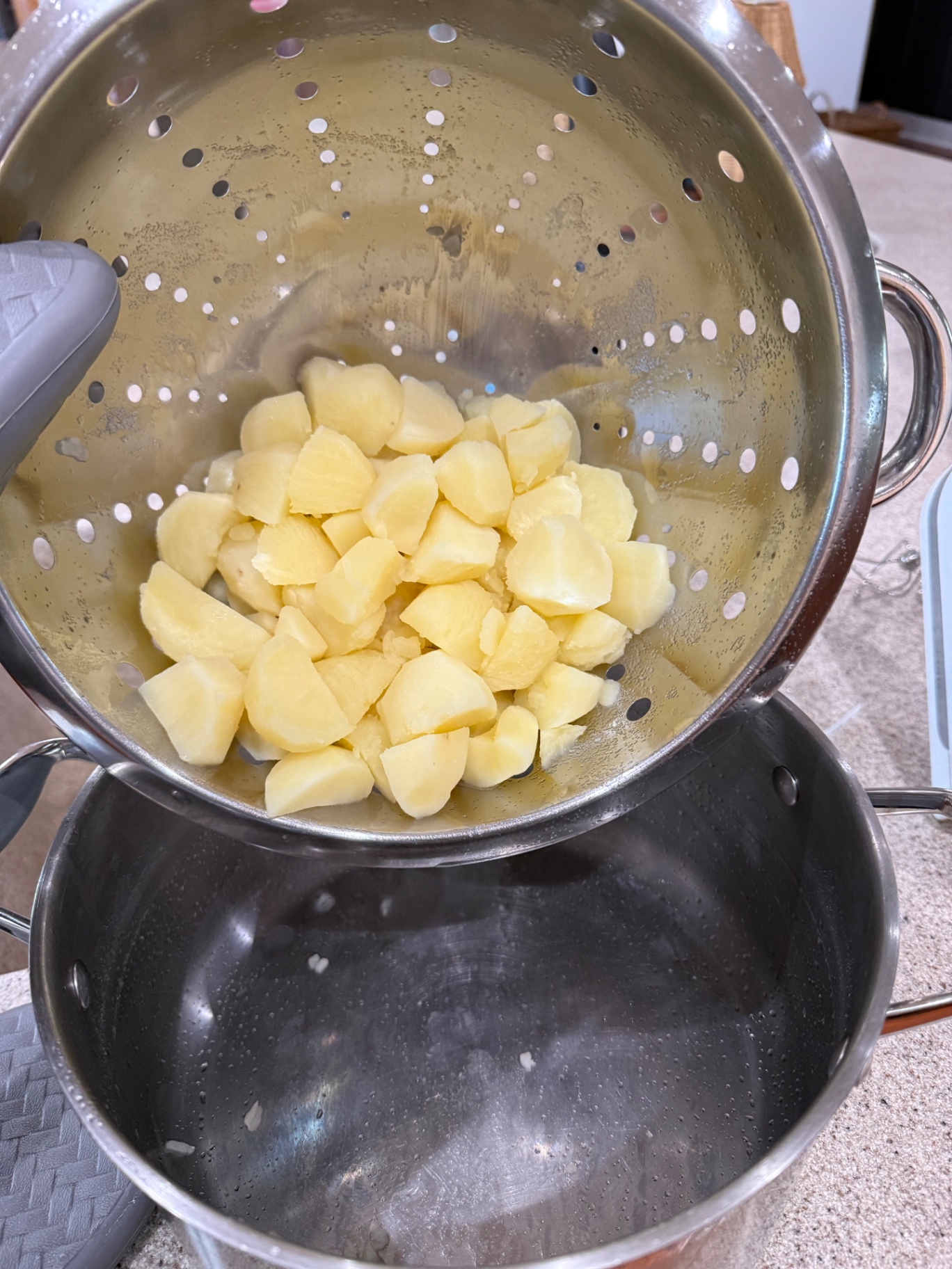Cooked potato chunks draining in a metal colander over the sink.