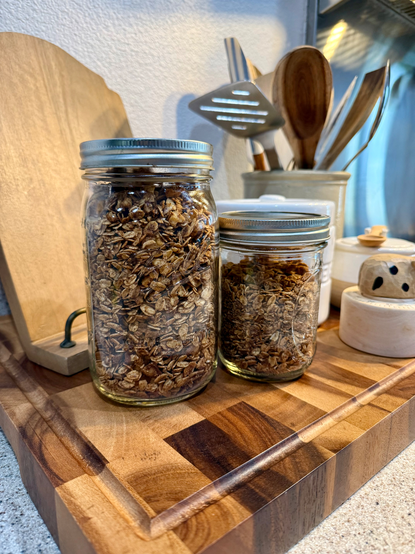 Homemade granola stored in two glass mason jars on a wooden cutting board.