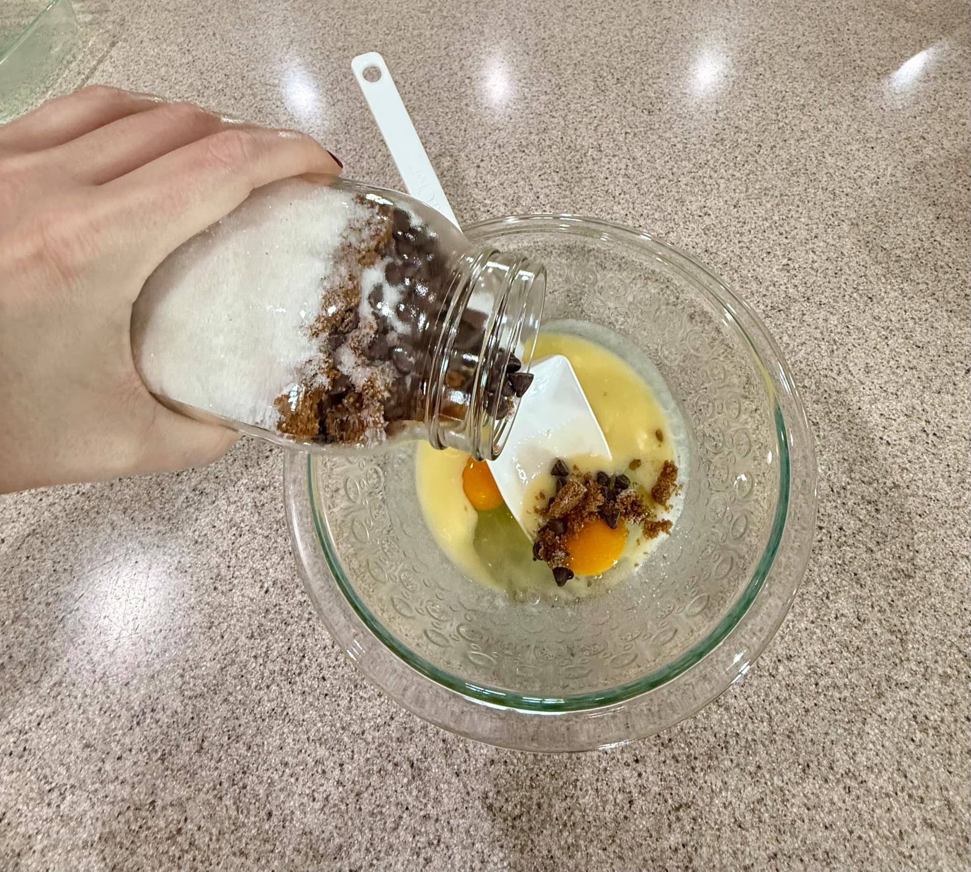Pouring the layered brownie mix from the mason jar into a glass bowl with melted butter and eggs.