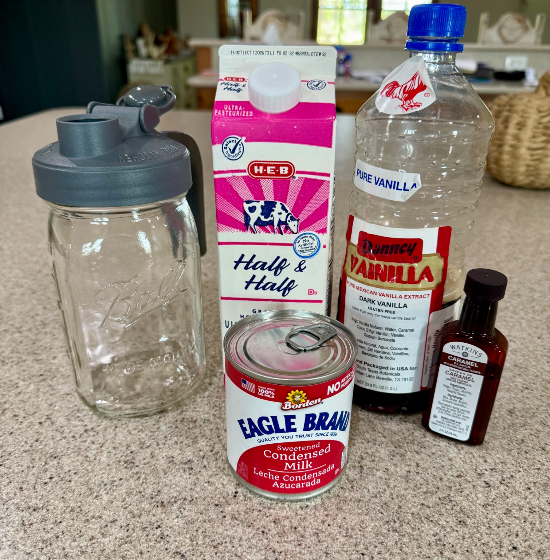 A Ball mason jar with a pour lid, half-and-half, sweetened condensed milk, vanilla extract, and caramel flavor on the kitchen counter.
