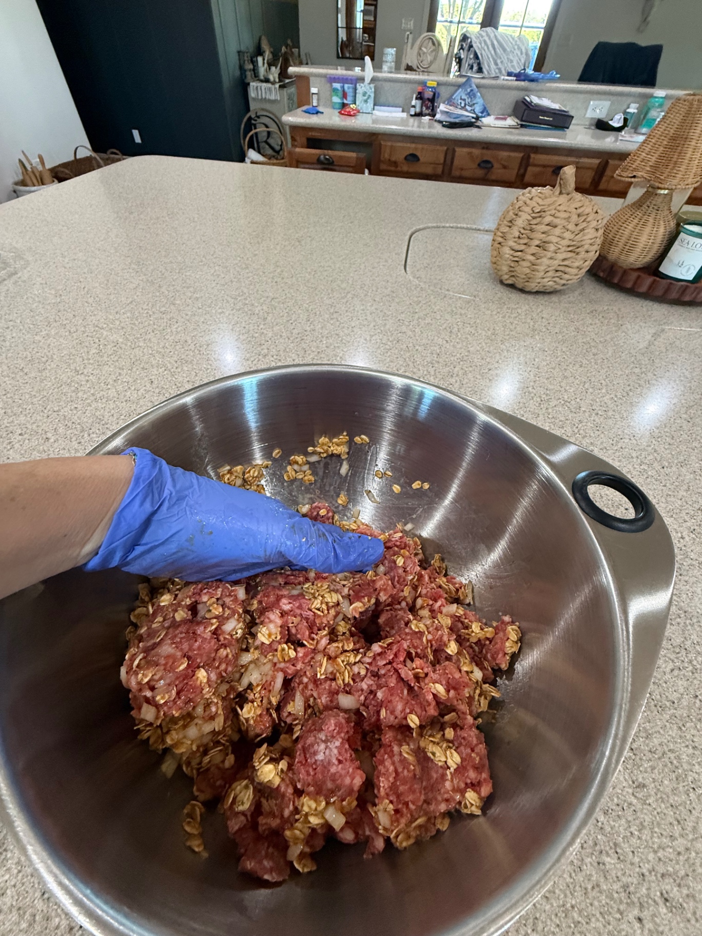 A gloved hand mixing ground beef, oats, and onion together in a stainless bowl.