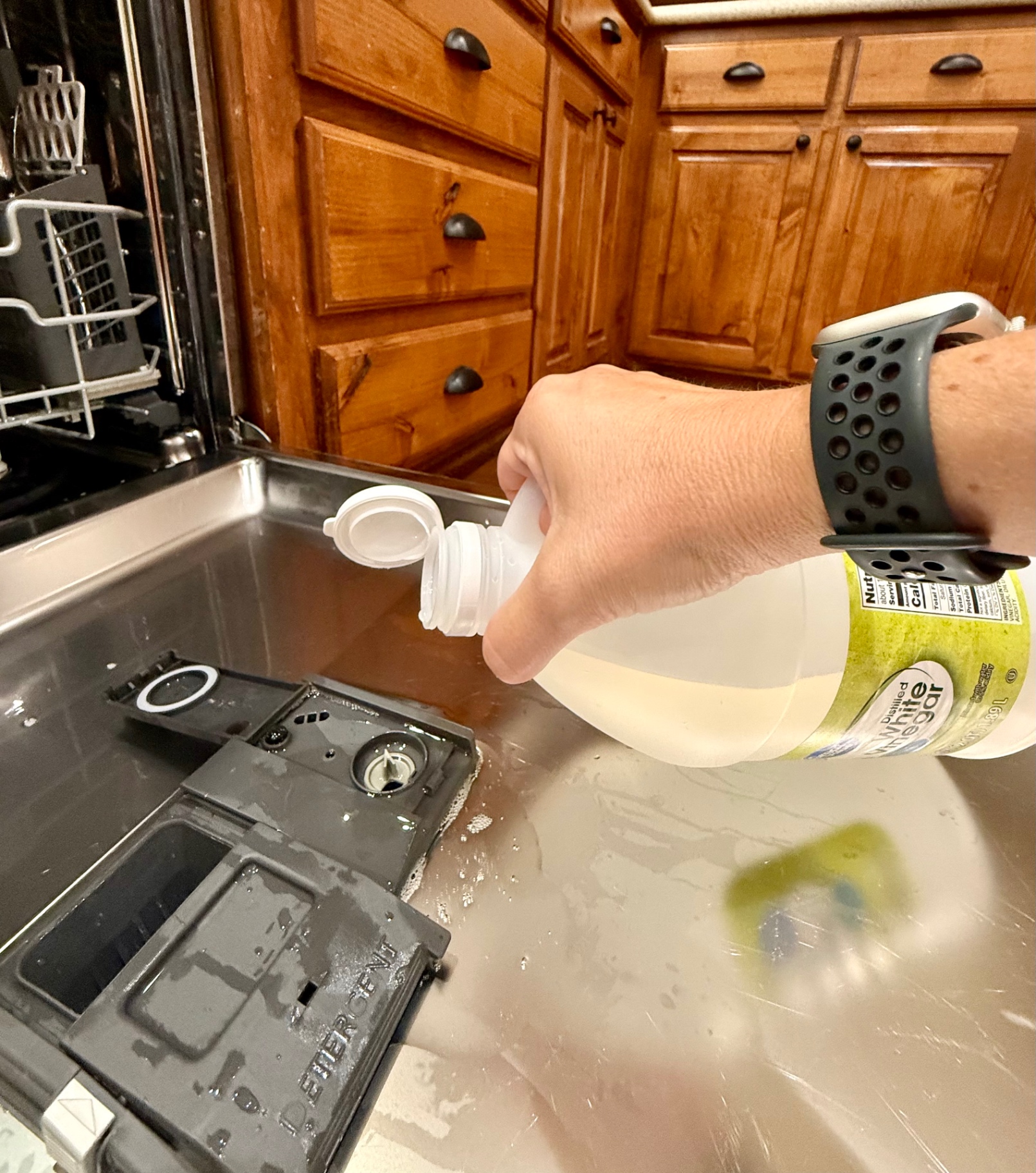 Pouring distilled white vinegar into a dishwasher rinse aid compartment.