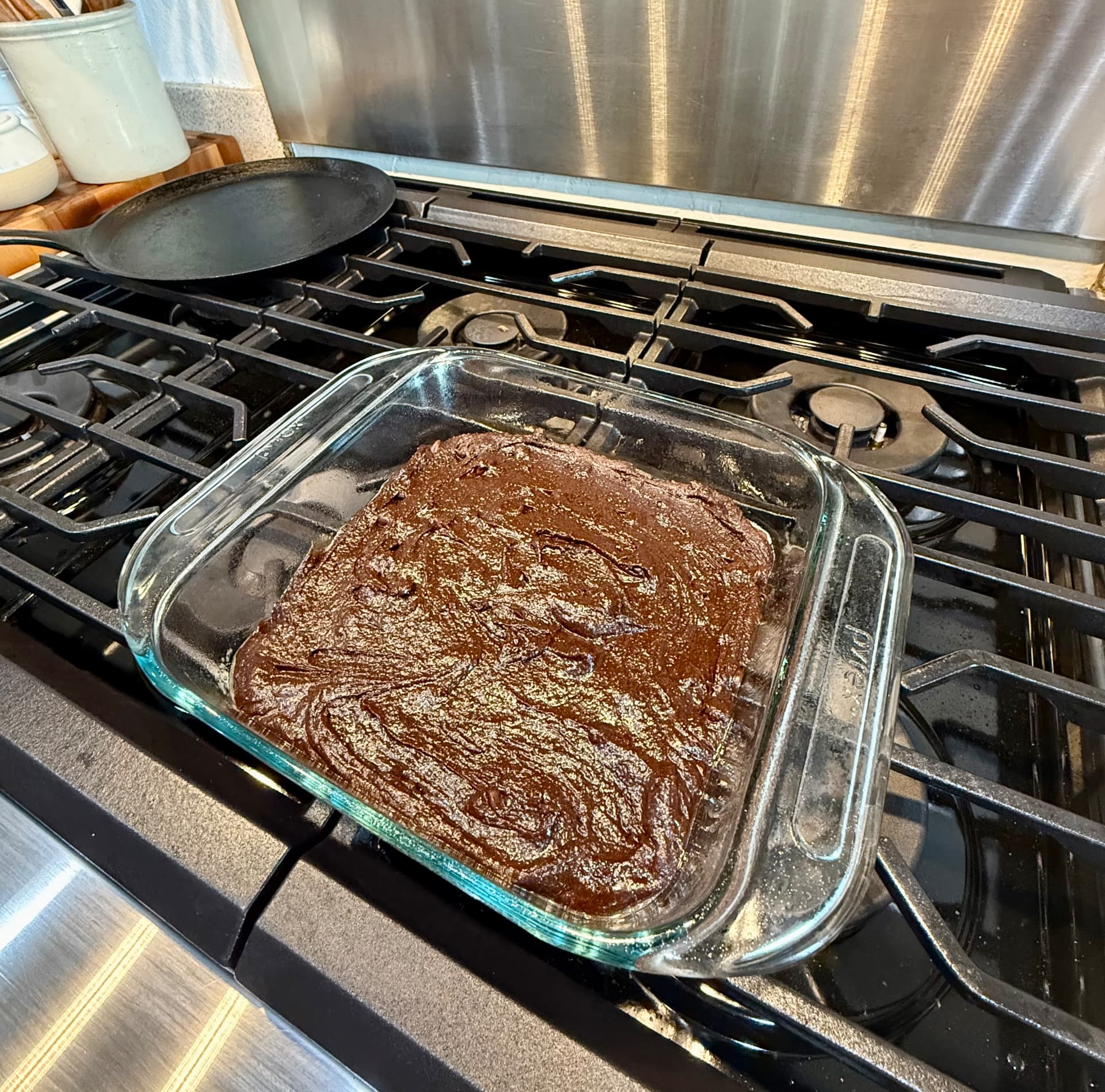 Brownie batter spread evenly in a square glass baking dish on the stovetop.