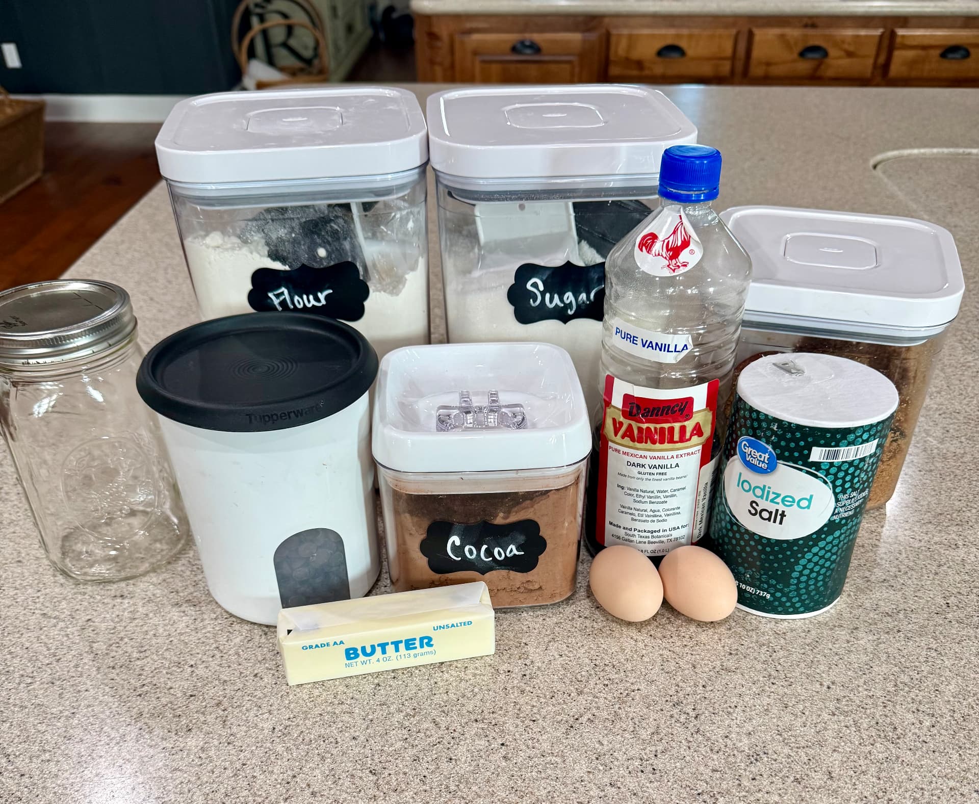 Flour, sugar, cocoa, brown sugar, chocolate chips, vanilla, salt, two eggs, a stick of unsalted butter, and an empty quart mason jar on the kitchen counter.
